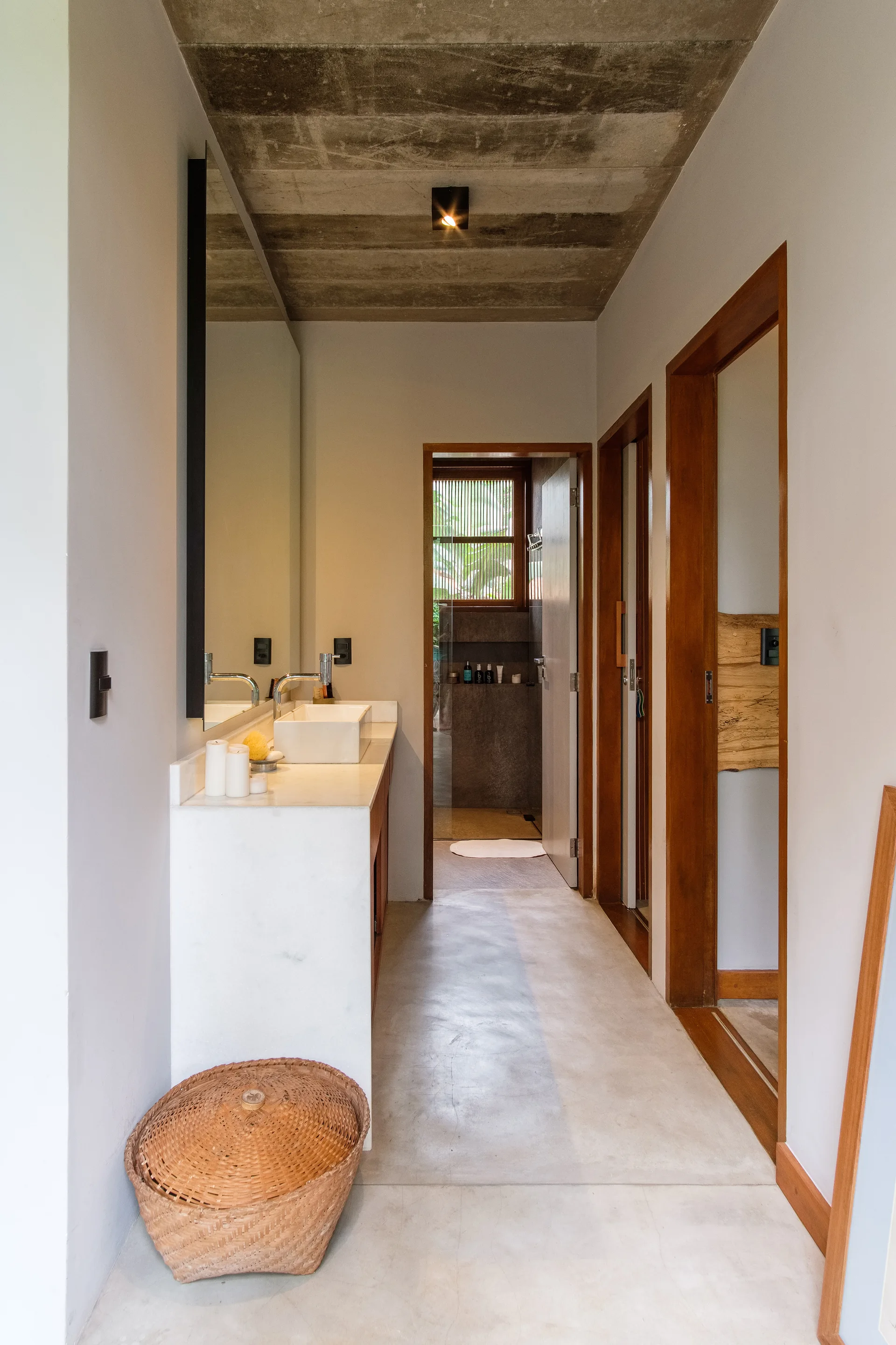 A minimalist bathroom featuring a white stone vanity with a vessel sink, a raw concrete ceiling, smooth gray floors, and warm wood door frames.