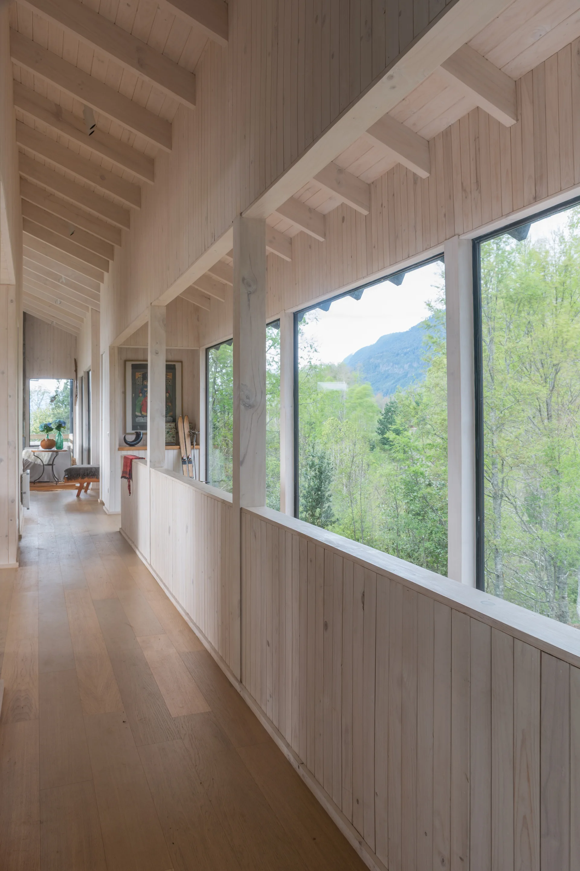 A long hallway lined with light vertical wood paneling, featuring large windows showing a mountain view and an exposed beam ceiling.