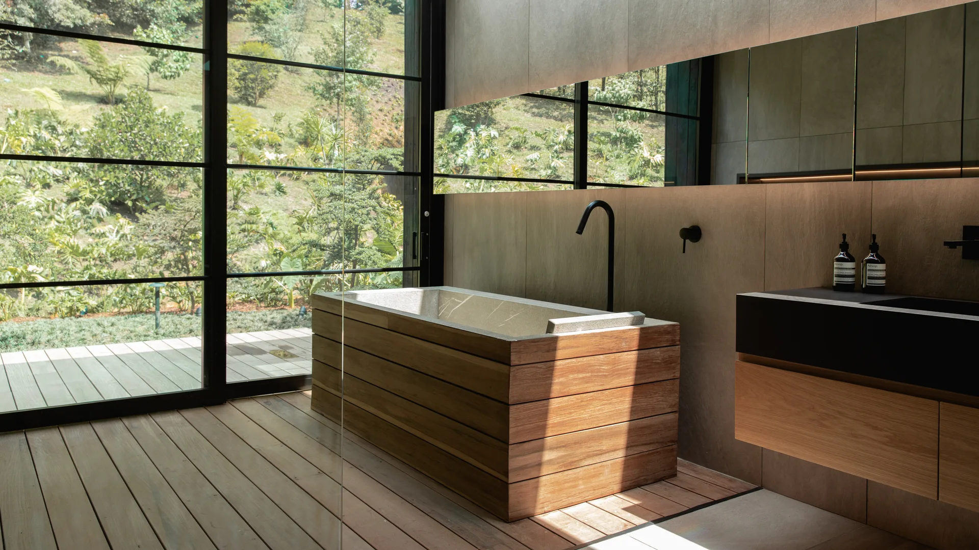 A modern bathroom featuring a rectangular wood-clad bathtub, a floating vanity, and floor-to-ceiling windows showing a lush green garden.