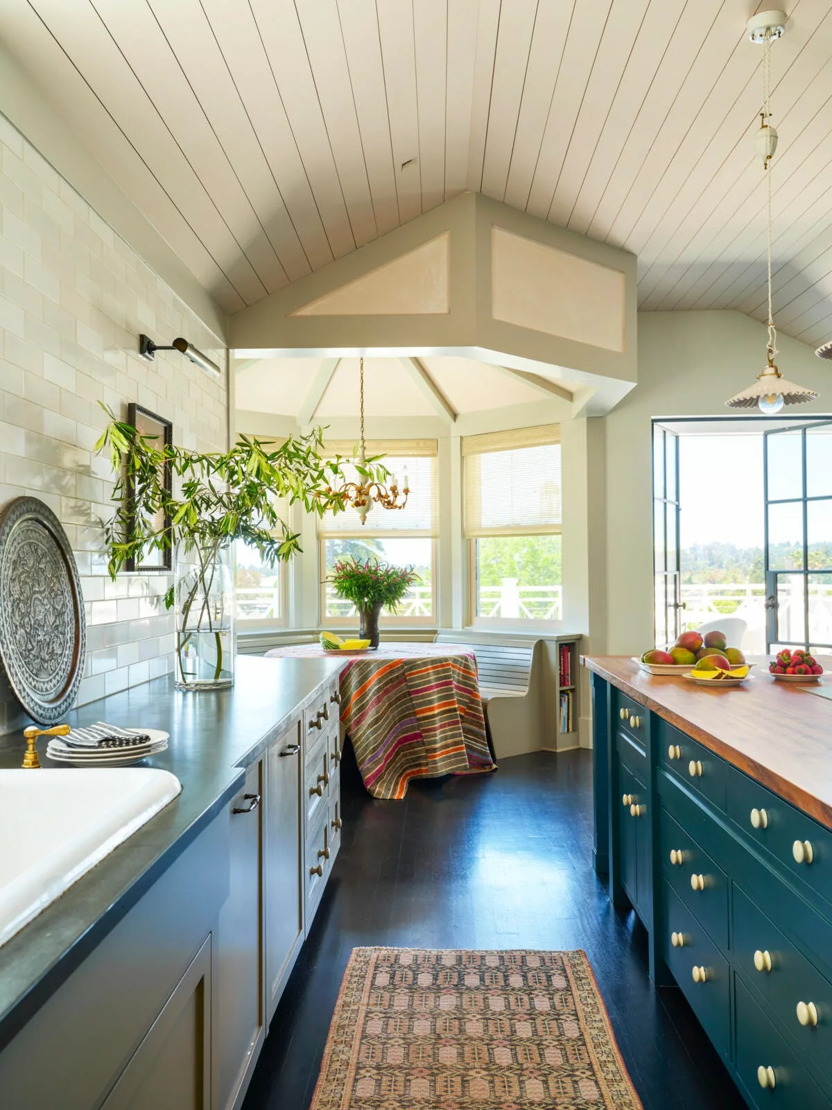 A kitchen featuring a dark green island with a wood countertop, a white tiled backsplash, and a bright breakfast nook with built-in bench seating.