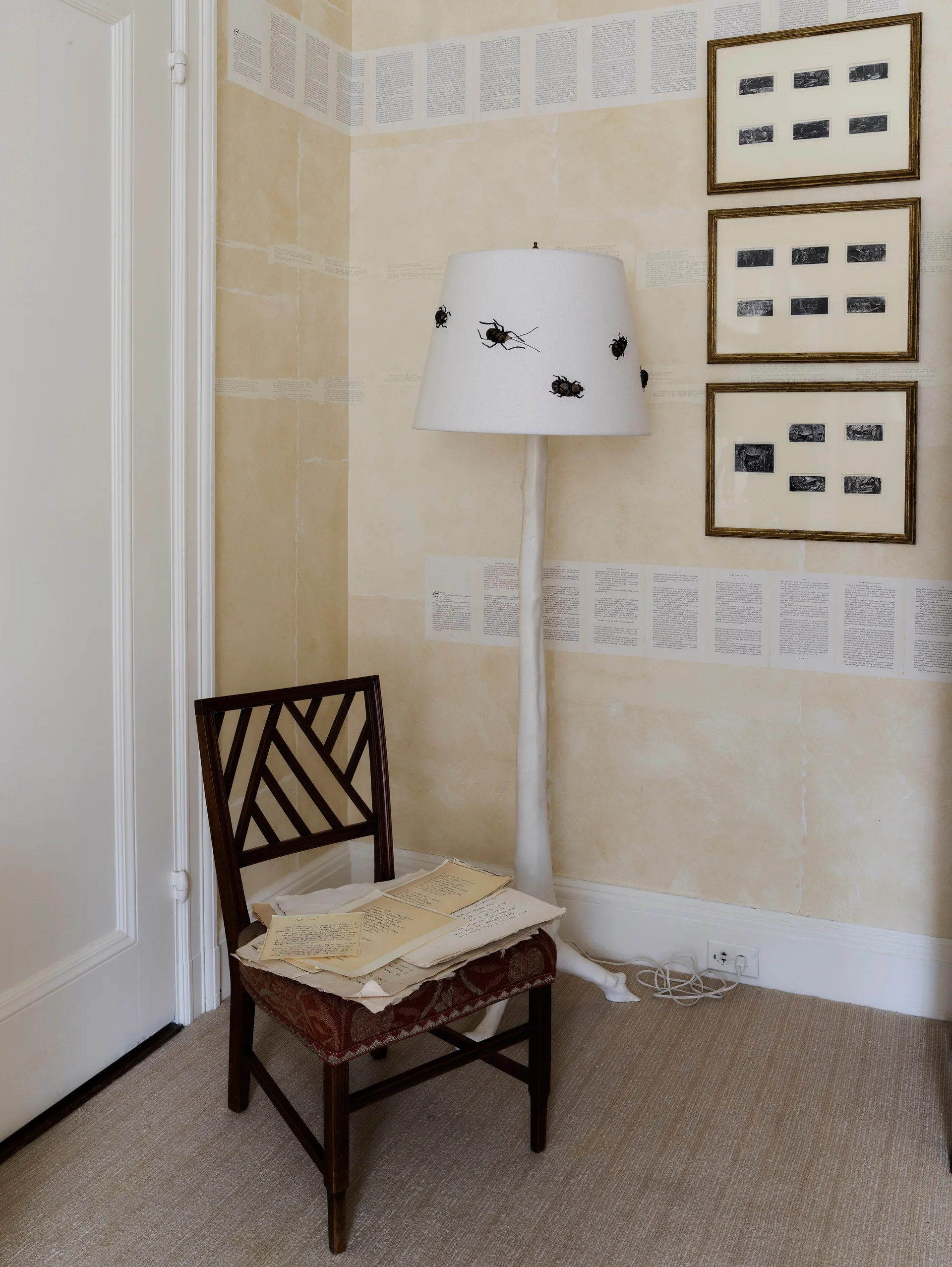 A wooden lattice-back chair sits next to a white floor lamp with insect accents against cream walls detailed with printed text strips.