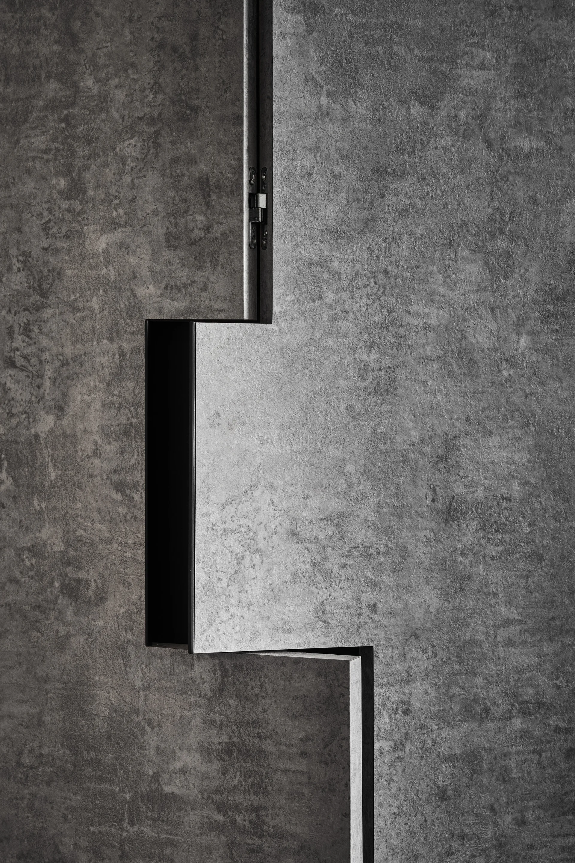 A close-up of dark gray stone-textured cabinet panels featuring a stepped interlocking shadow gap and a partially visible metal hinge.