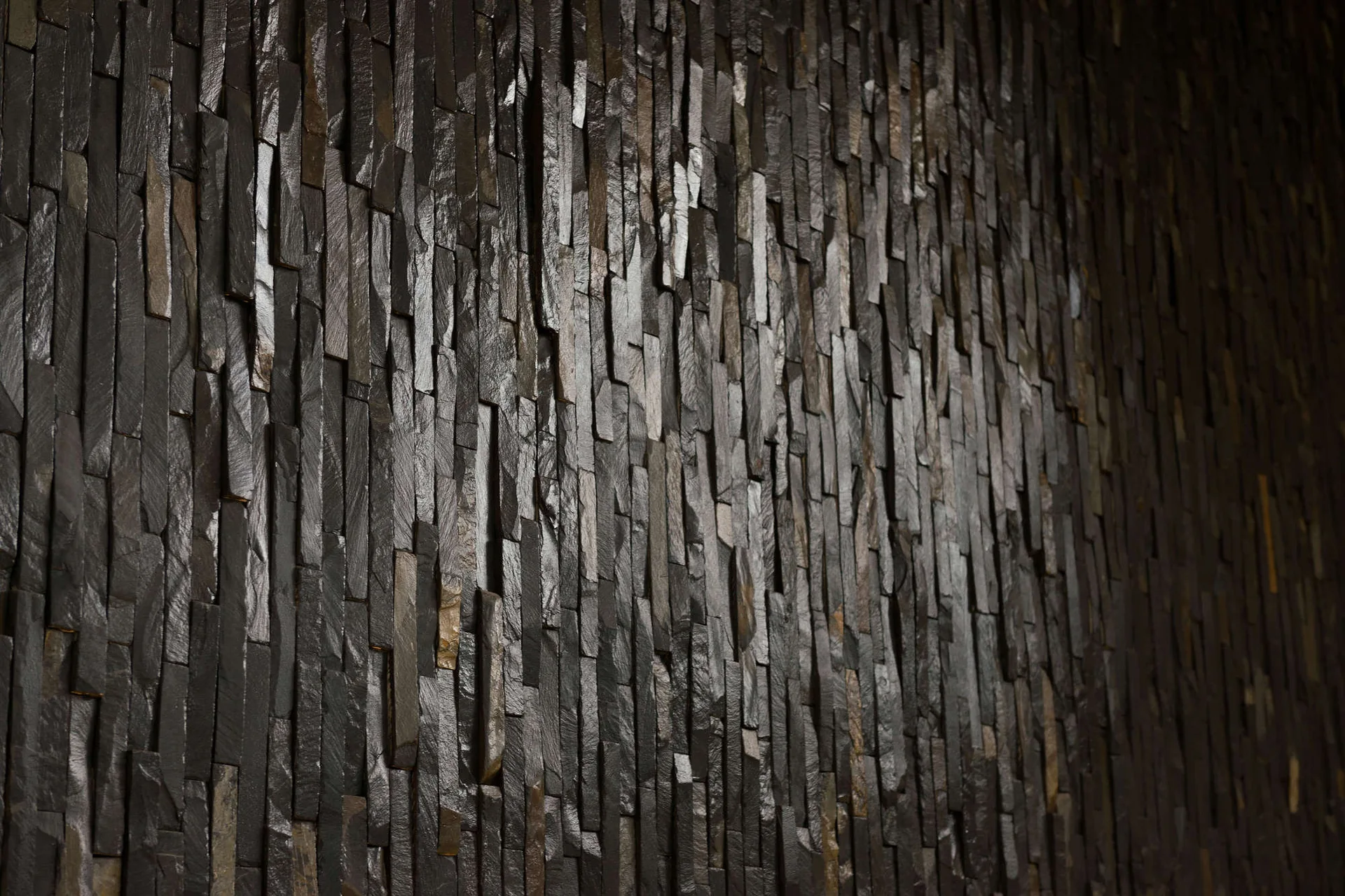A close-up view of textured dark grey and brown stacked stone wall cladding arranged in a vertical linear pattern.