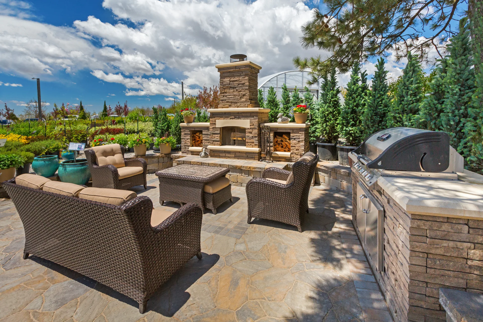 A spacious outdoor flagstone patio features a built-in stone fireplace with wood storage niches, wicker patio chairs, and an integrated grill station.