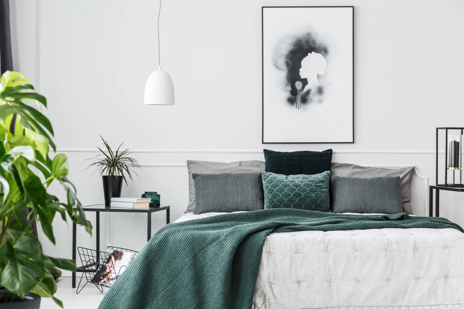 A modern minimalist bedroom featuring a bed with green and grey linens, a black frame nightstand, and framed silhouette wall art.