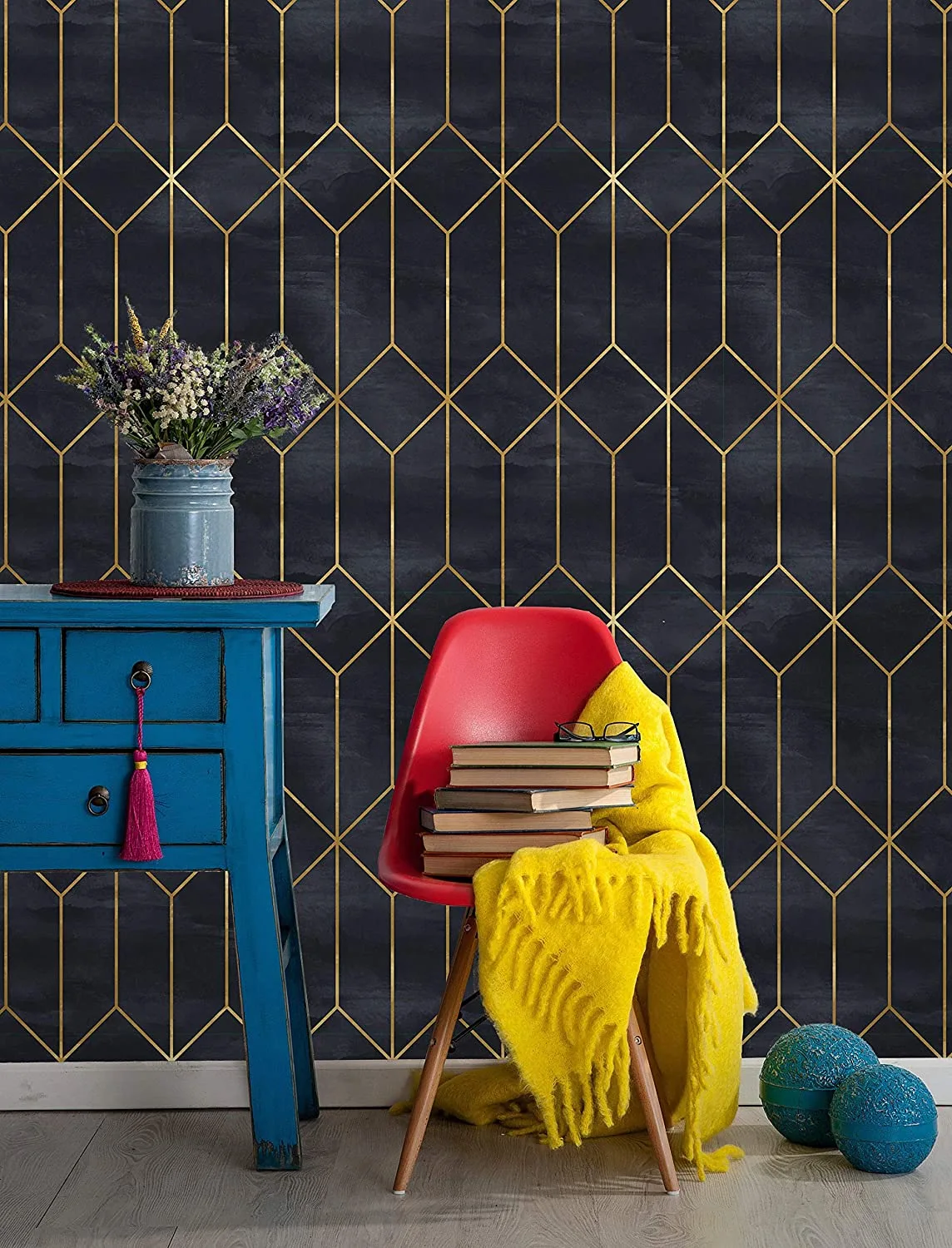 A blue wooden console table and a red molded plastic chair stand against dark navy wallpaper featuring a gold geometric diamond pattern.