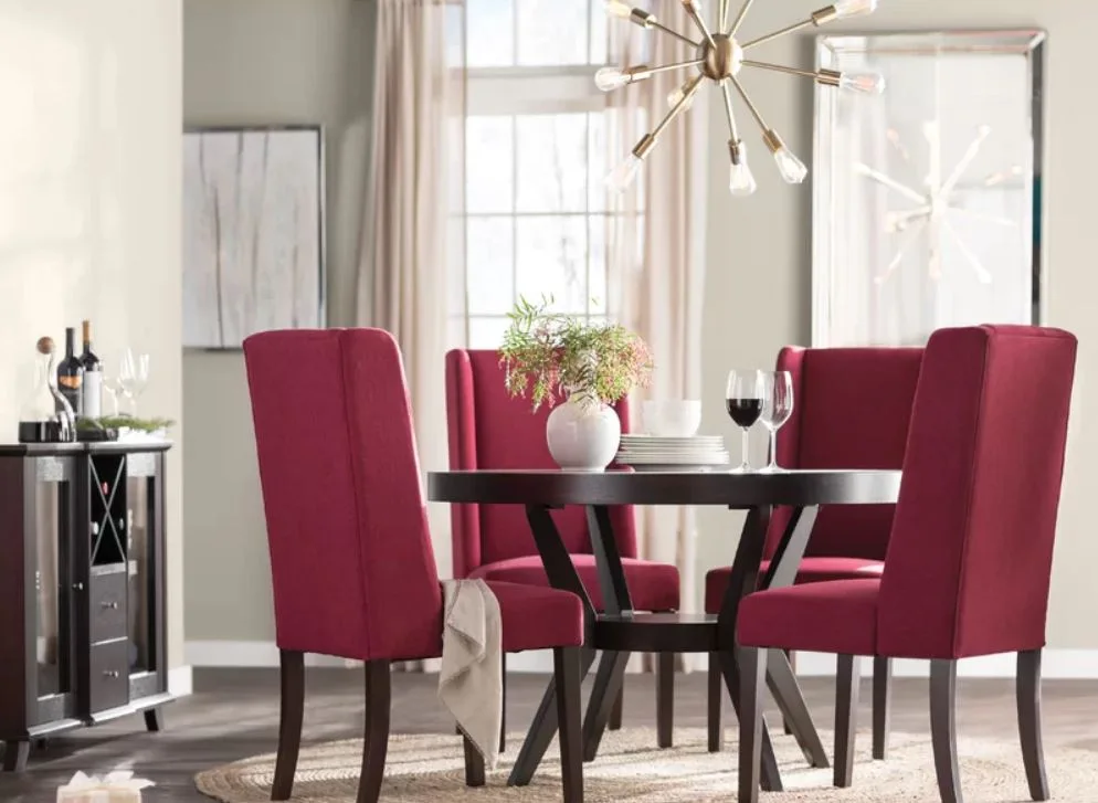 A dark wood circular dining table surrounded by four maroon upholstered chairs under a brass sputnik chandelier in a neutral-toned room.