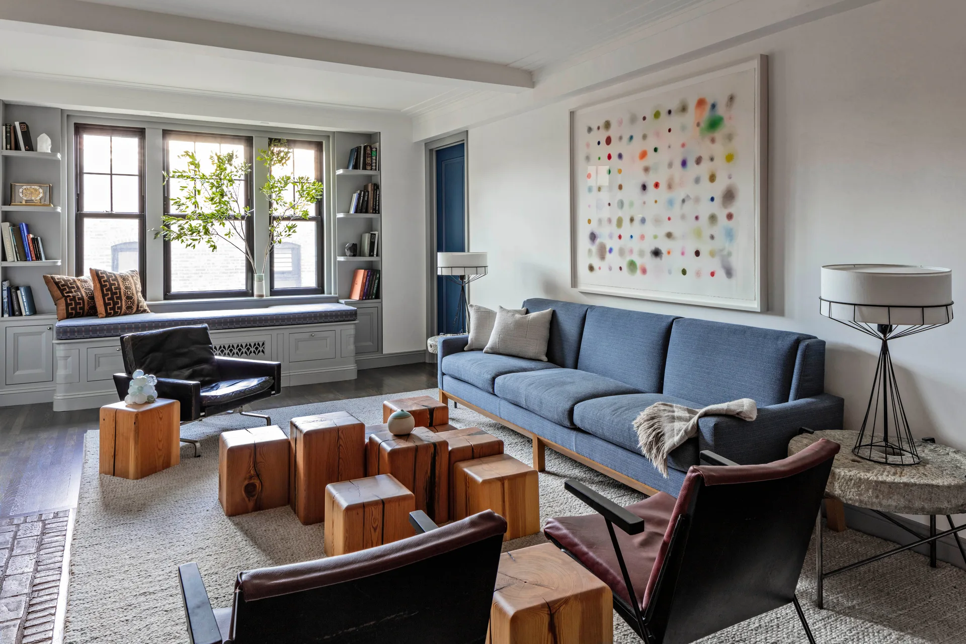 A living room features a blue sofa, leather armchairs, and a clustered wooden block coffee table on a textured neutral rug.