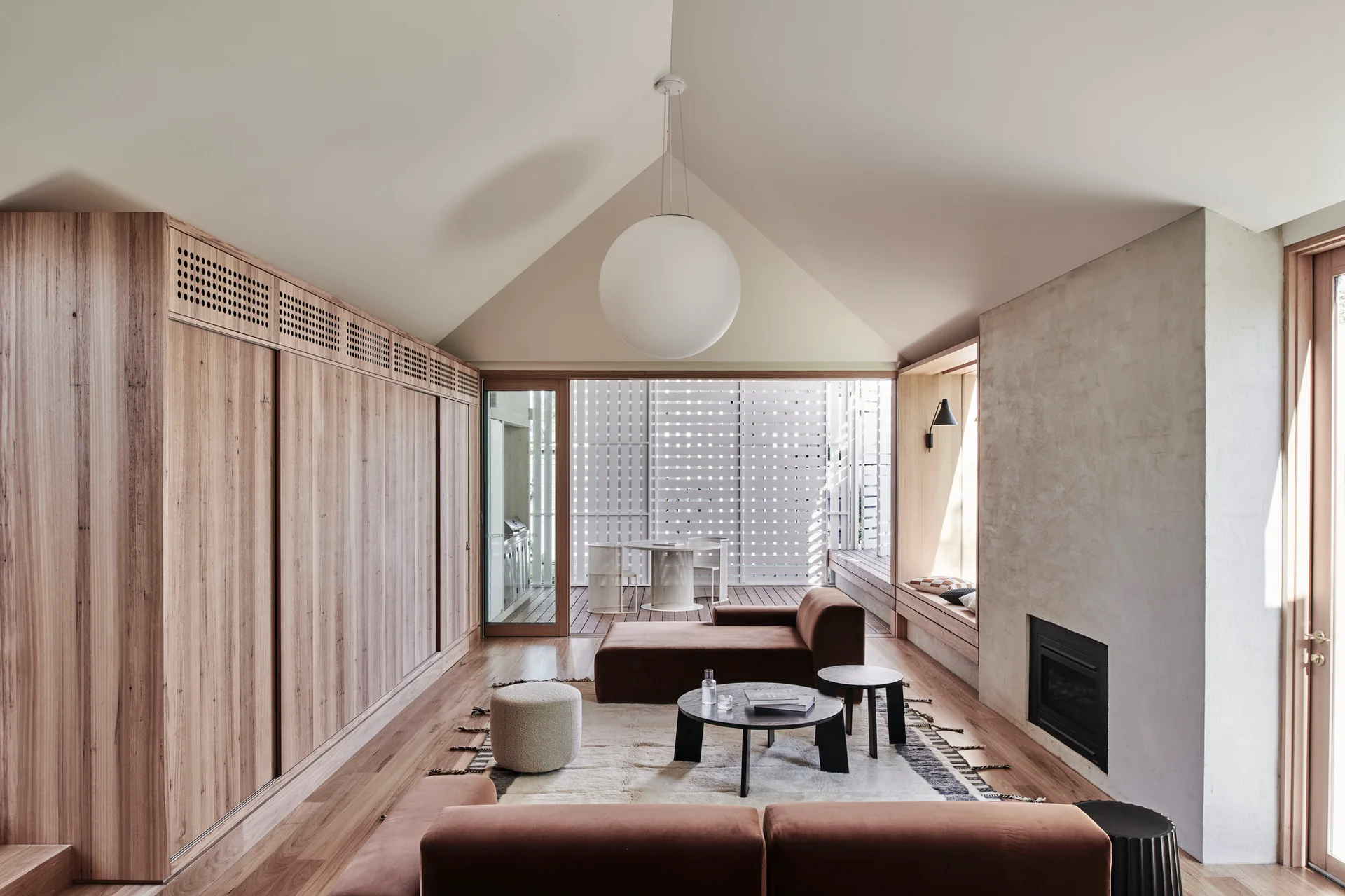 A minimalist living room features a vaulted ceiling, a large globe pendant light, brown velvet sofas, and a wall of built-in wooden cabinetry.