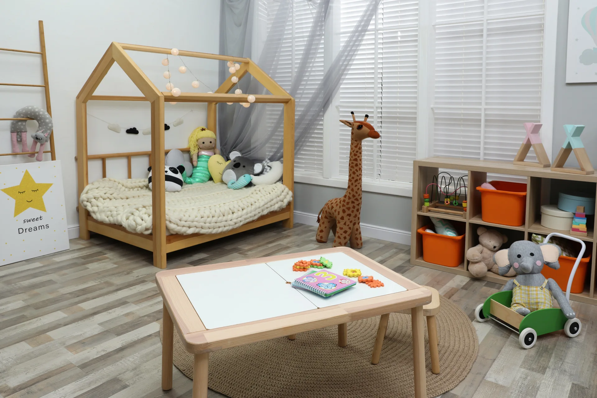 A children's playroom features a wooden house-shaped bed, a low activity table, a round jute rug, and a cube storage shelf.