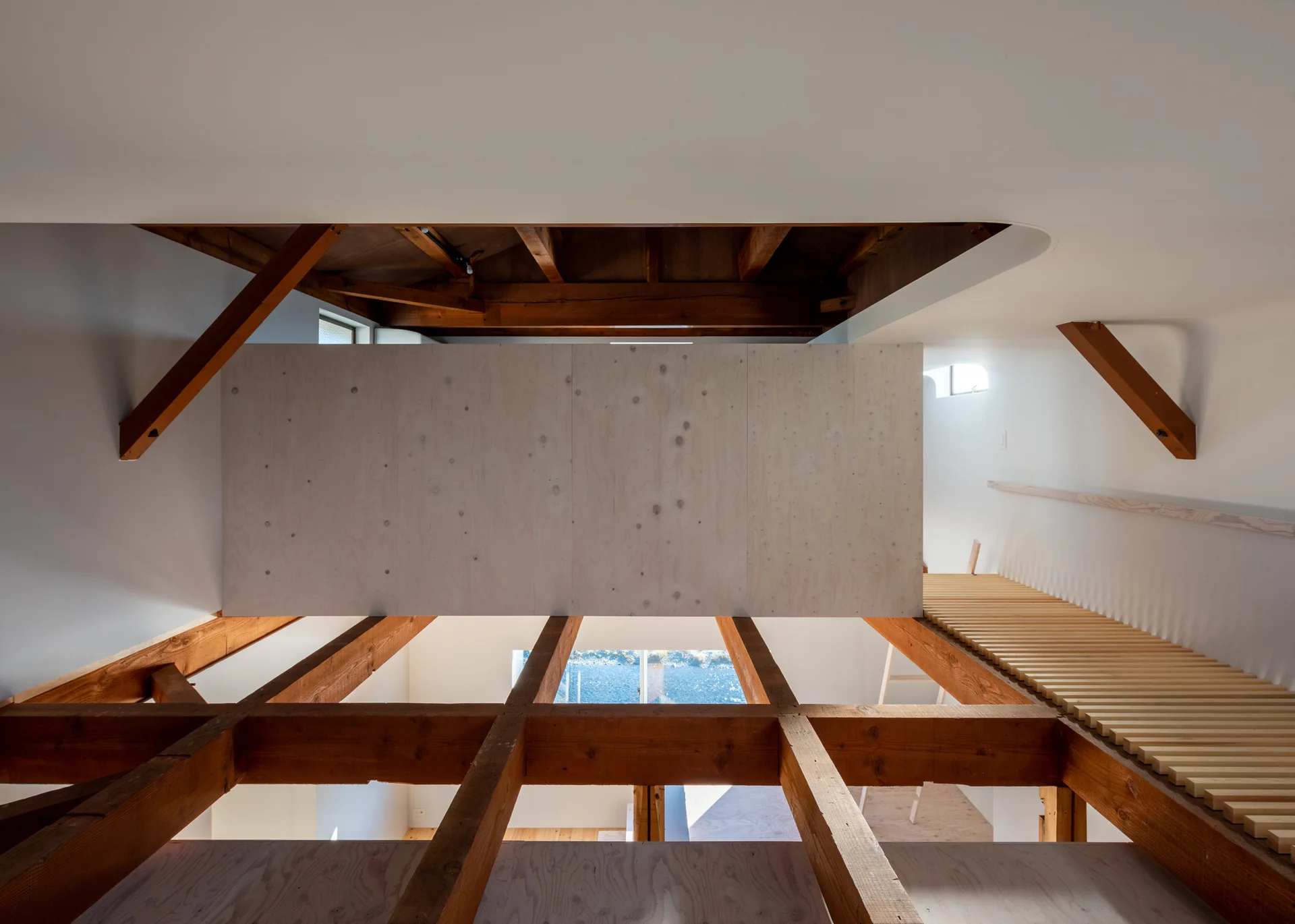 An architectural view of a modern loft showing exposed wooden structural beams, a large pale plywood panel, and a light-colored wooden slat walkway.