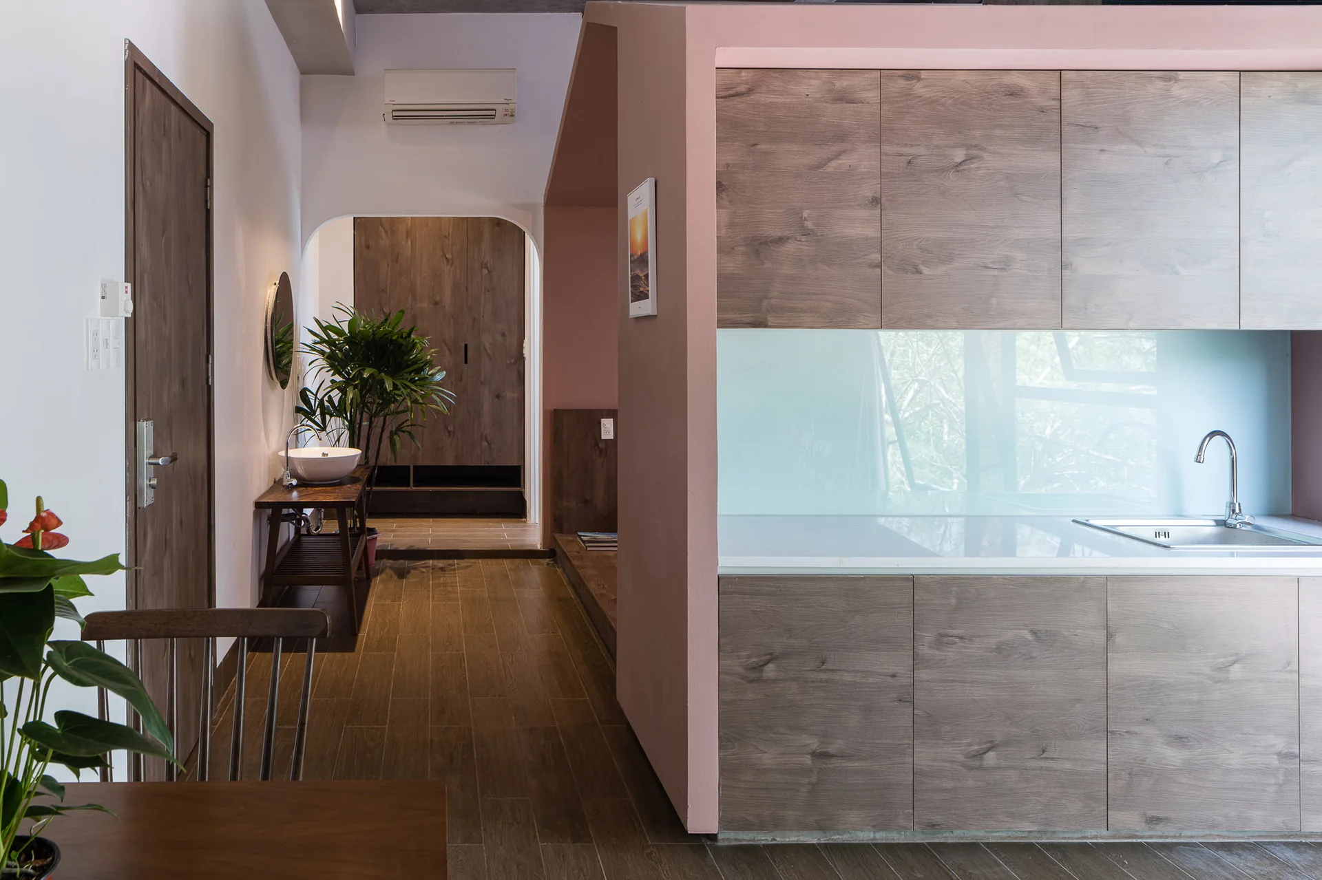 A kitchen with wood-grained cabinets and a pink partition wall next to an arched entryway with a second basin sink.