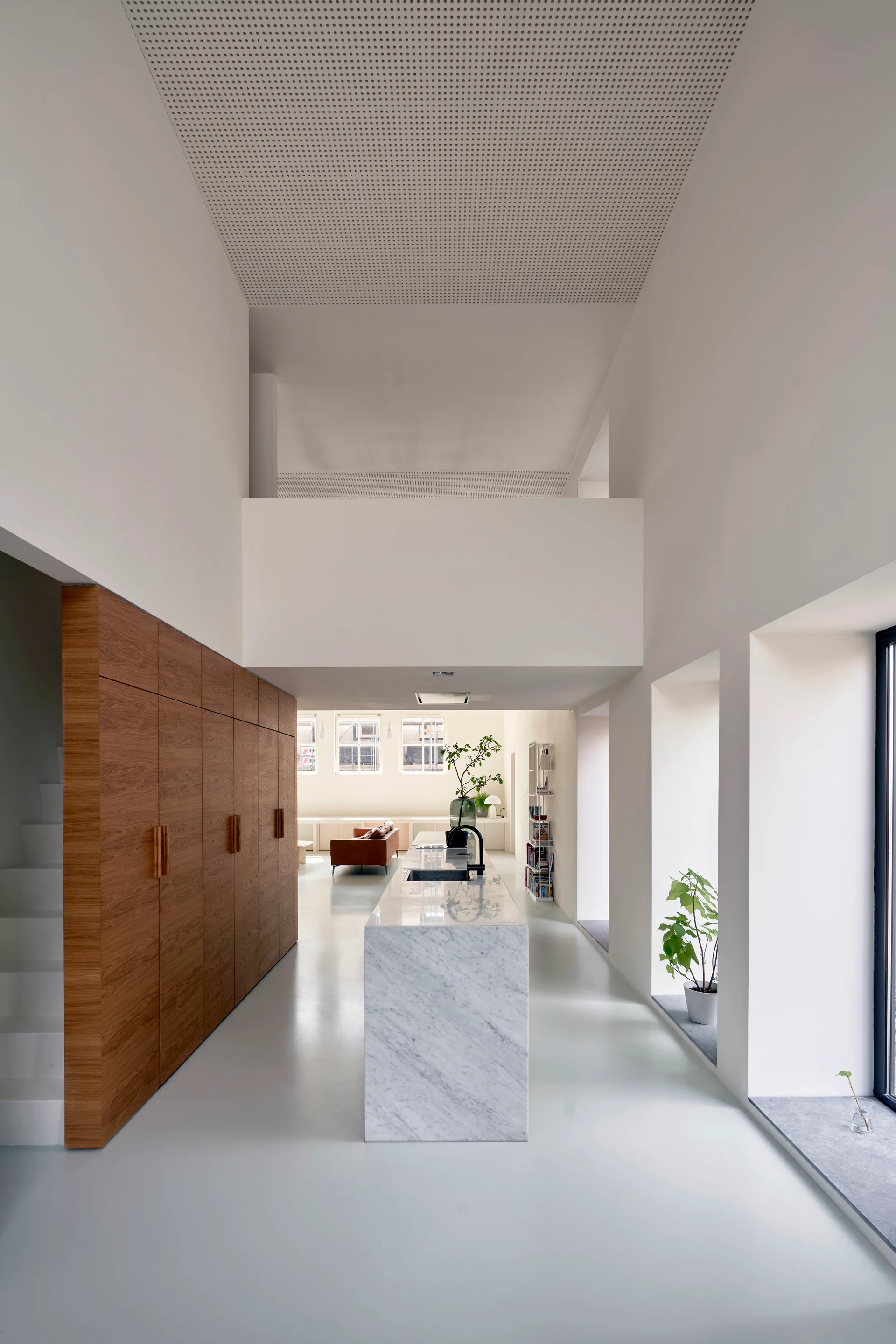 A minimalist kitchen featuring a central marble-topped island, full-height warm wood storage cabinets, and a double-height white ceiling.