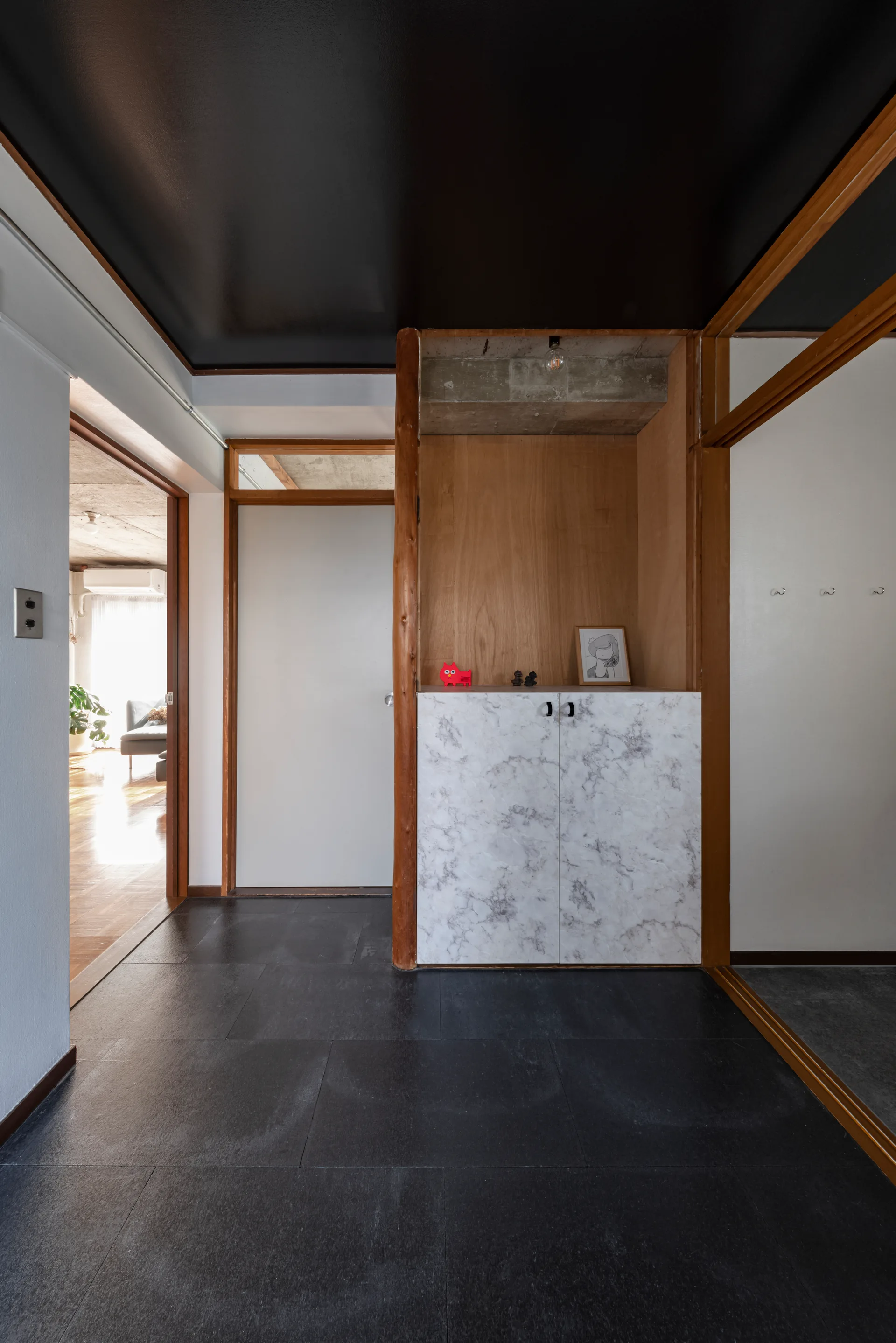 A modern entryway features a black ceiling, dark floor tiles, and a wooden niche housing a built-in cabinet with marble-patterned doors.
