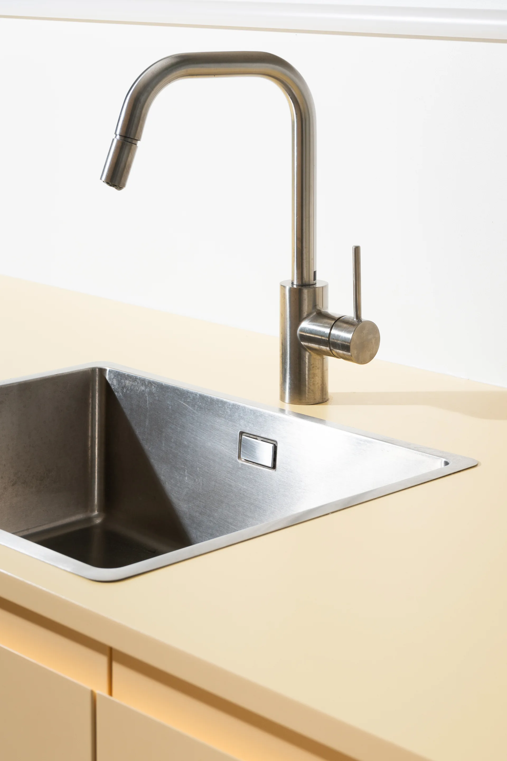 A close-up of a brushed stainless steel gooseneck faucet and matching rectangular sink set into a smooth light yellow countertop.
