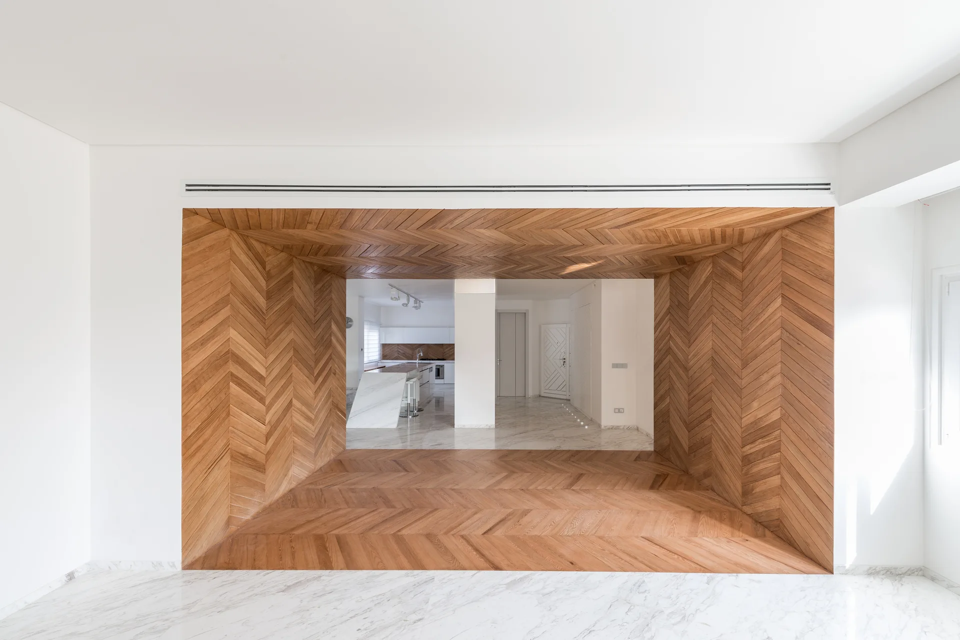 A large rectangular passageway clad entirely in herringbone-patterned wood transitions between white rooms with polished grey-veined marble floors.