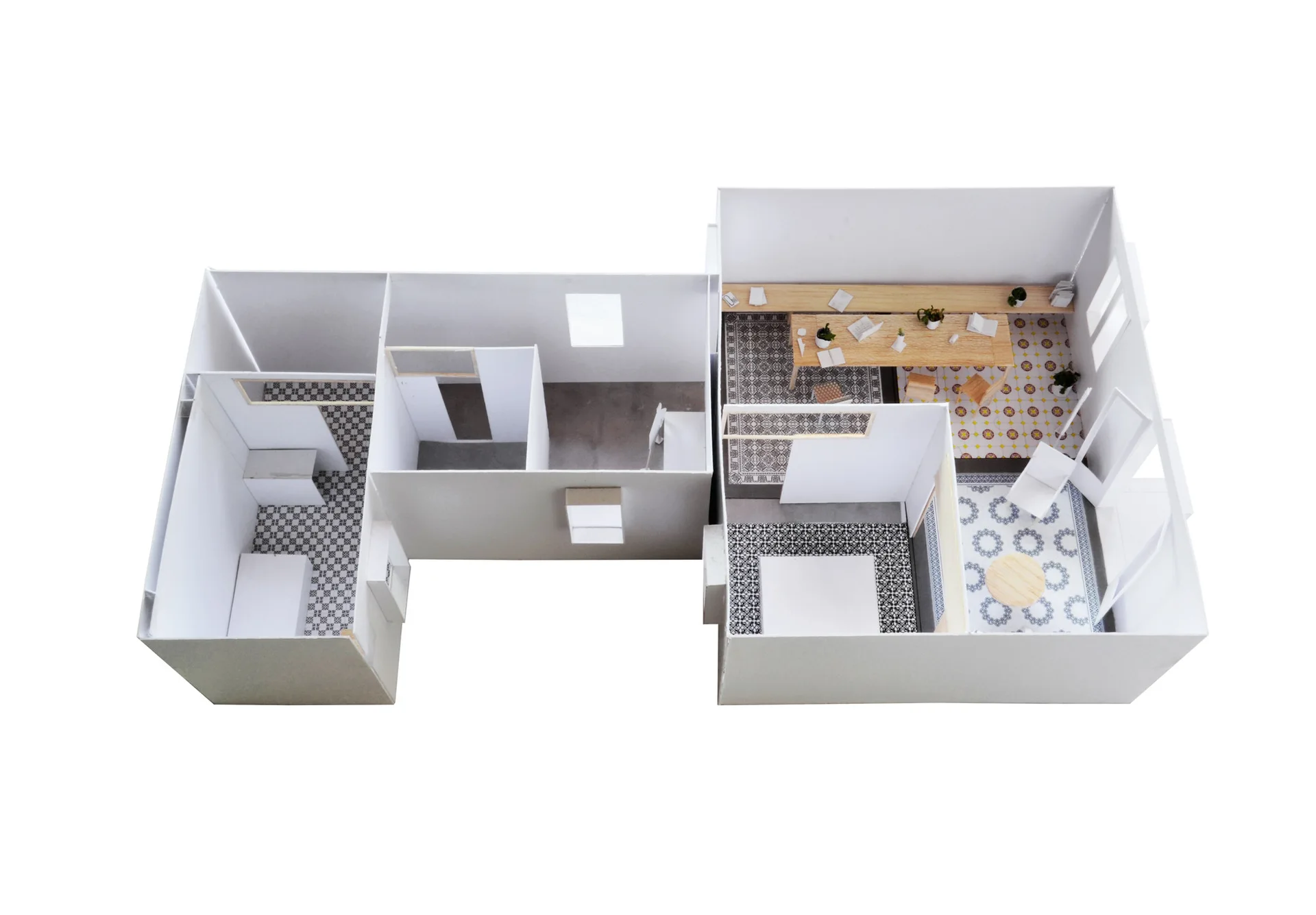 An architectural scale model of a multi-room layout featuring white walls, miniature wooden furniture, and various geometric patterned tile floors.