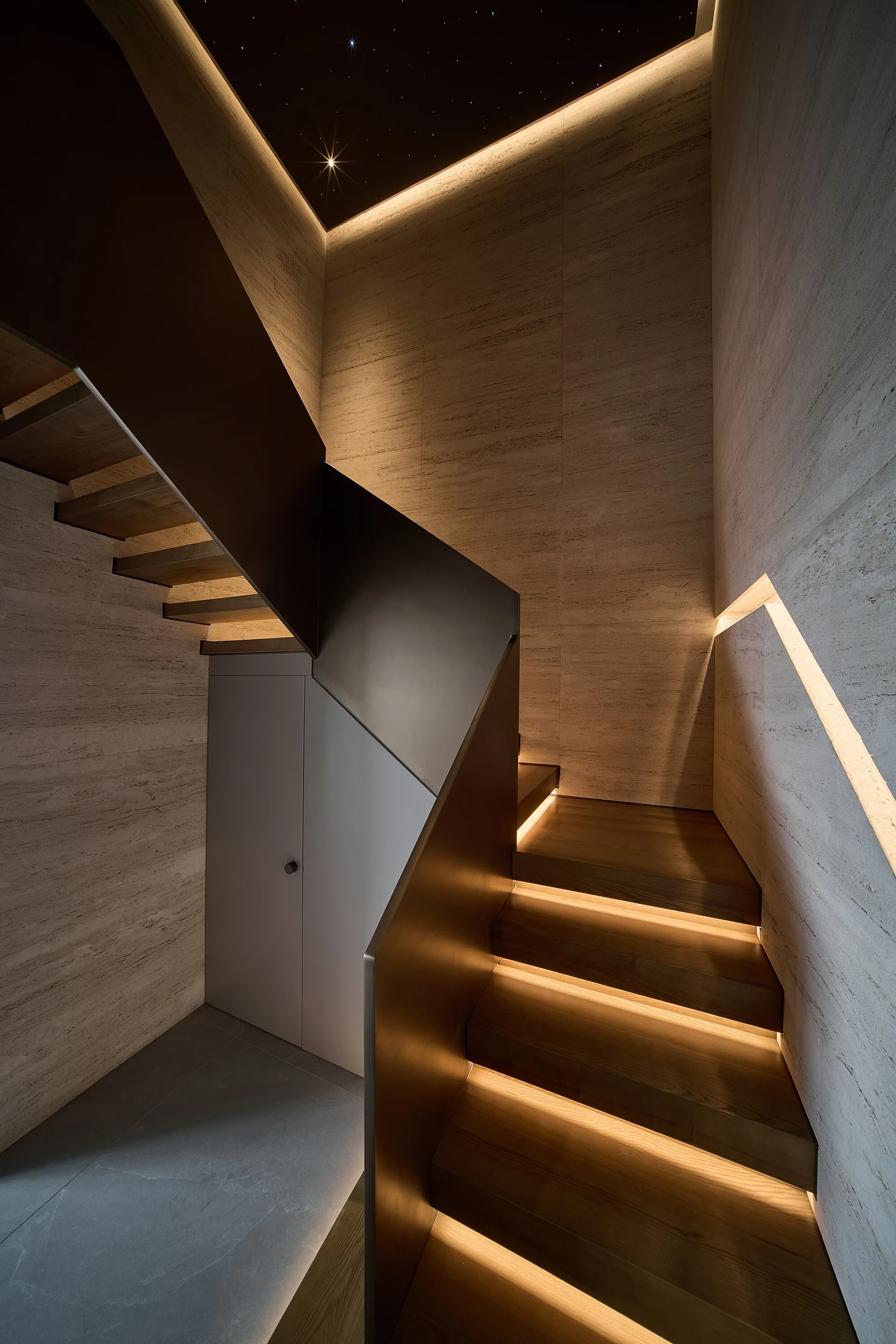 A modern wooden staircase with lighted treads, a dark metal banister, stone textured walls, and a starry ceiling design.