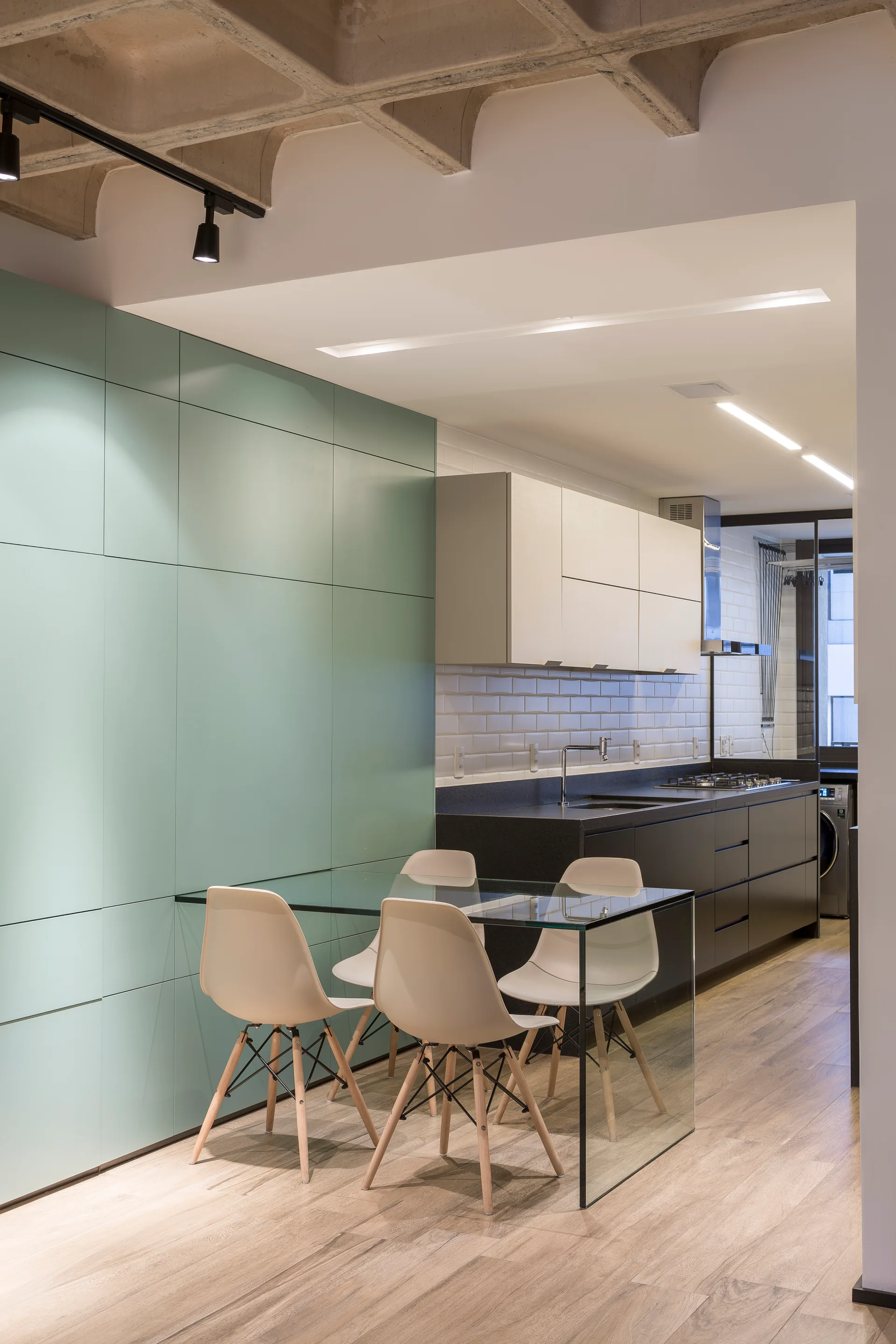 A modern kitchen and dining space with mint green cabinets, a transparent glass dining table, and an exposed concrete waffle ceiling.