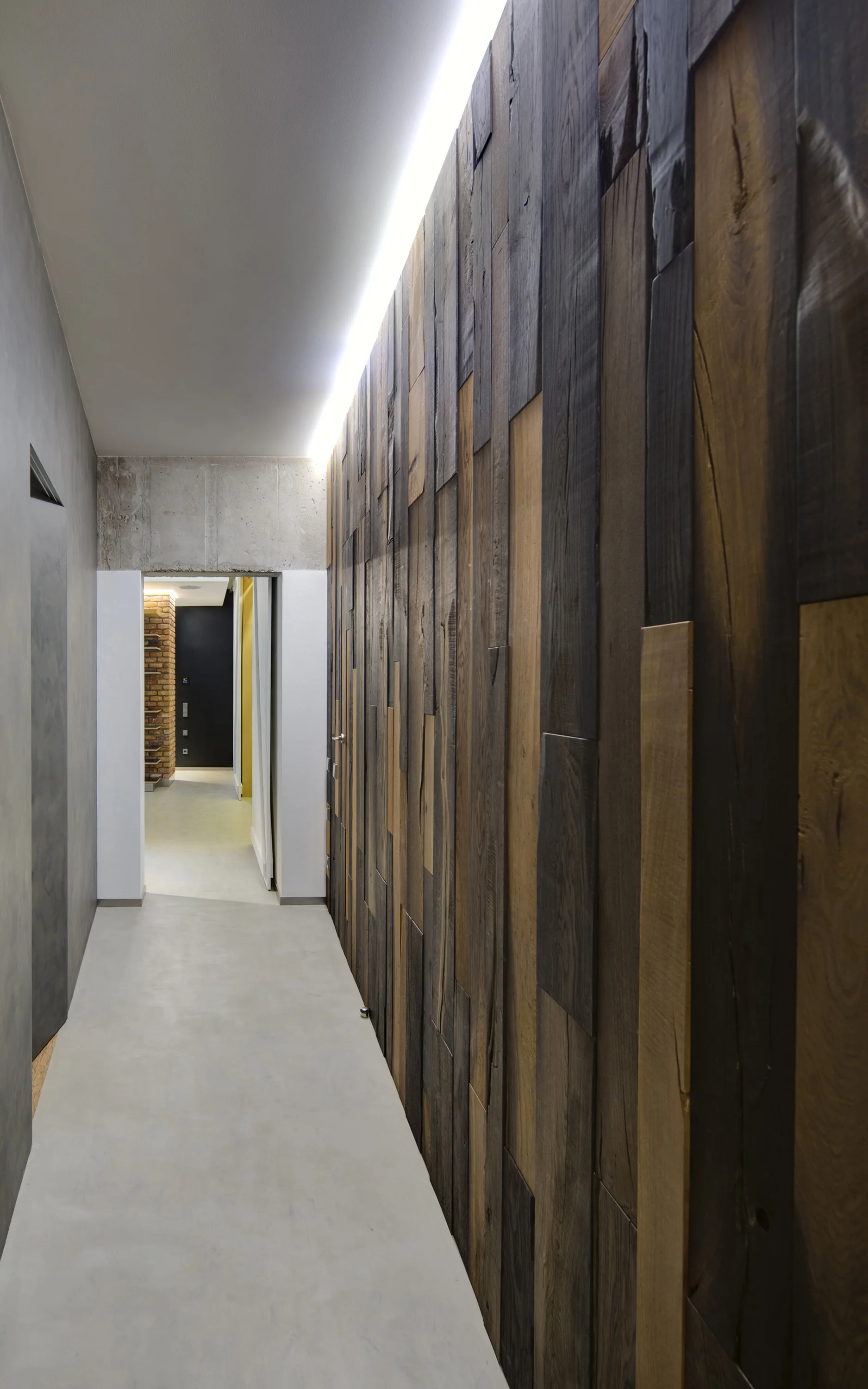A minimalist hallway featuring a multi-toned vertical wood plank feature wall, concrete flooring, and bright cove lighting along the ceiling.