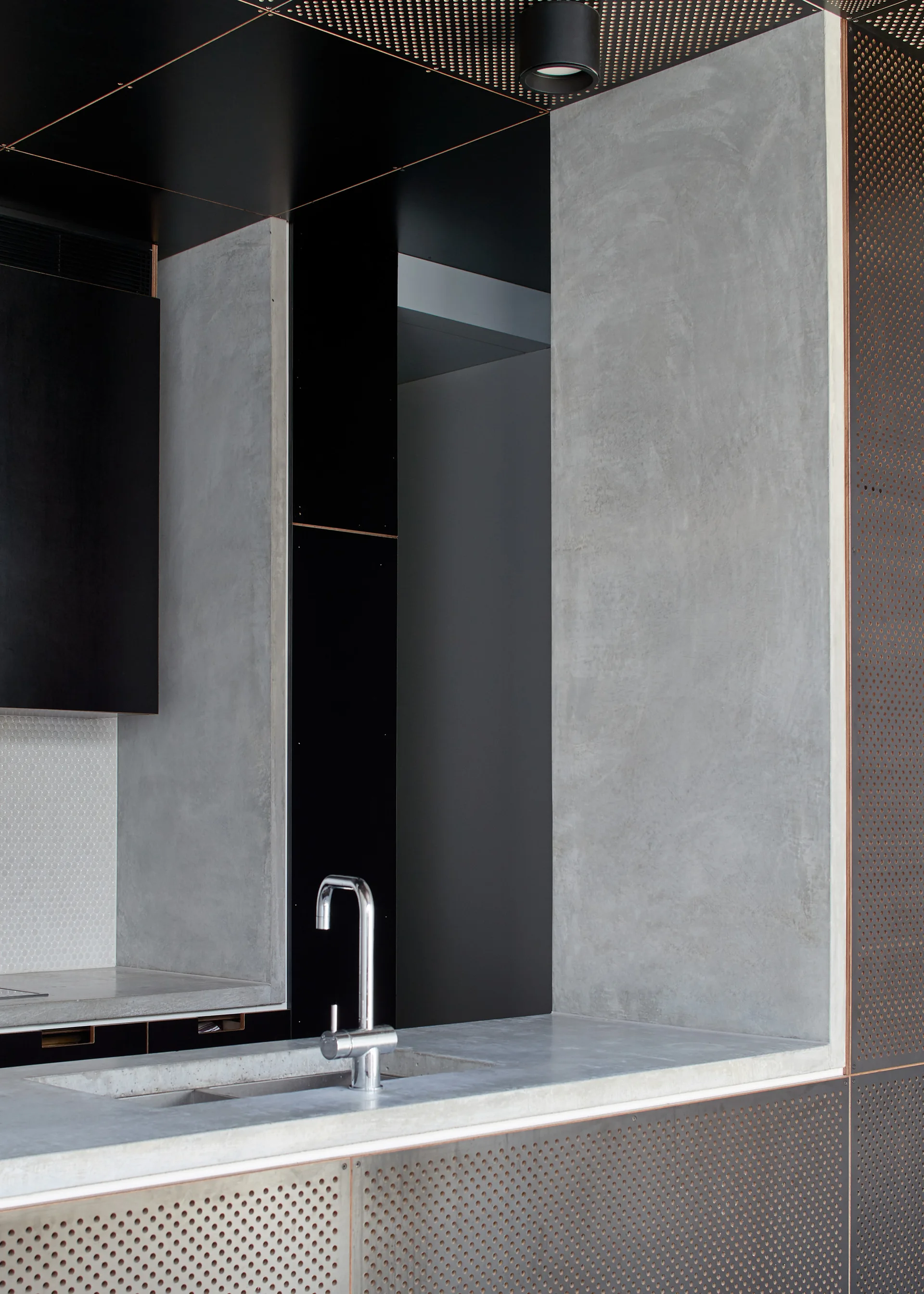 A close-up view of a modern kitchen featuring a concrete countertop with an integrated sink and chrome faucet next to perforated metal wall panels.