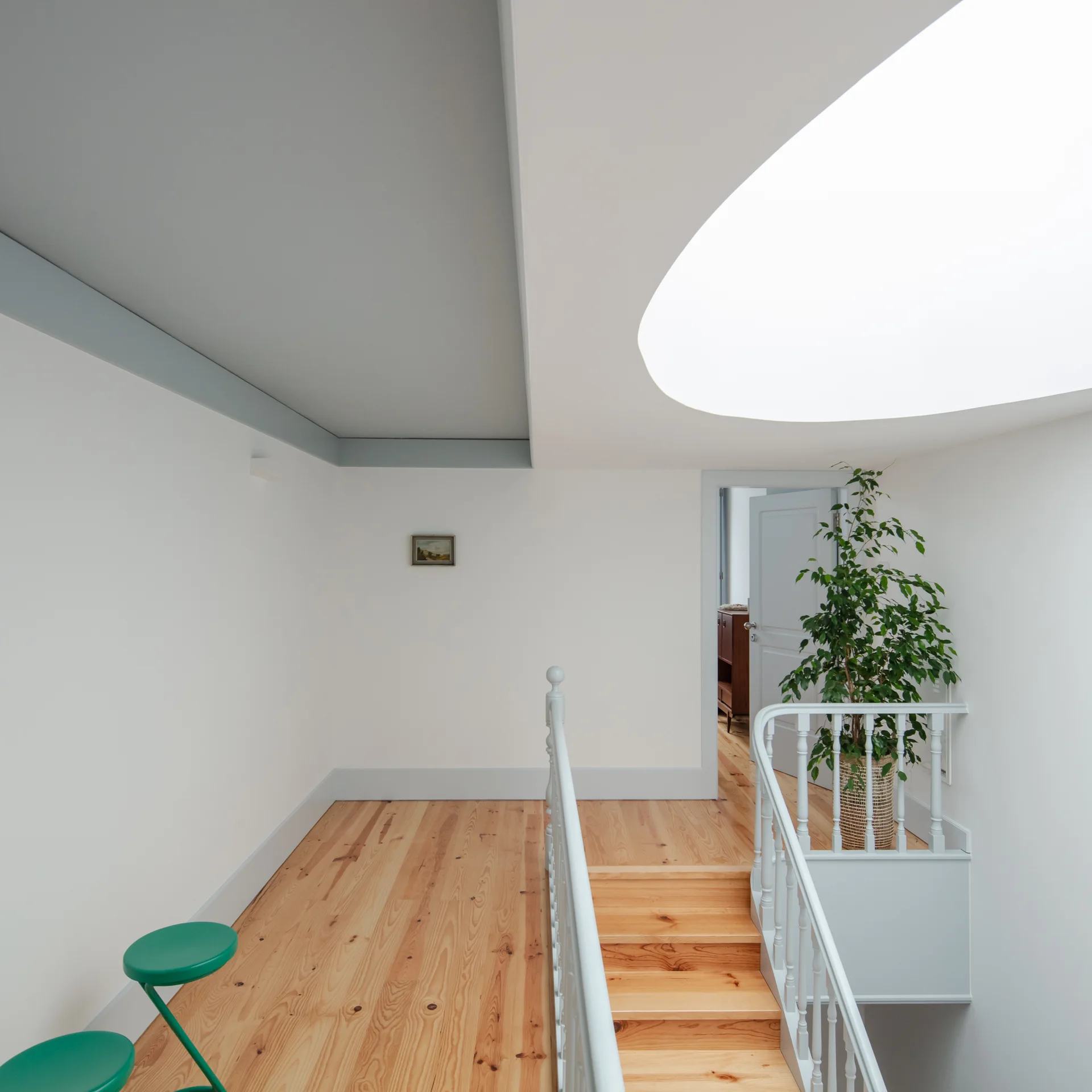 A light-filled hallway landing with natural pine floors, a white staircase railing, a large curved skylight, and a grey ceiling inset.