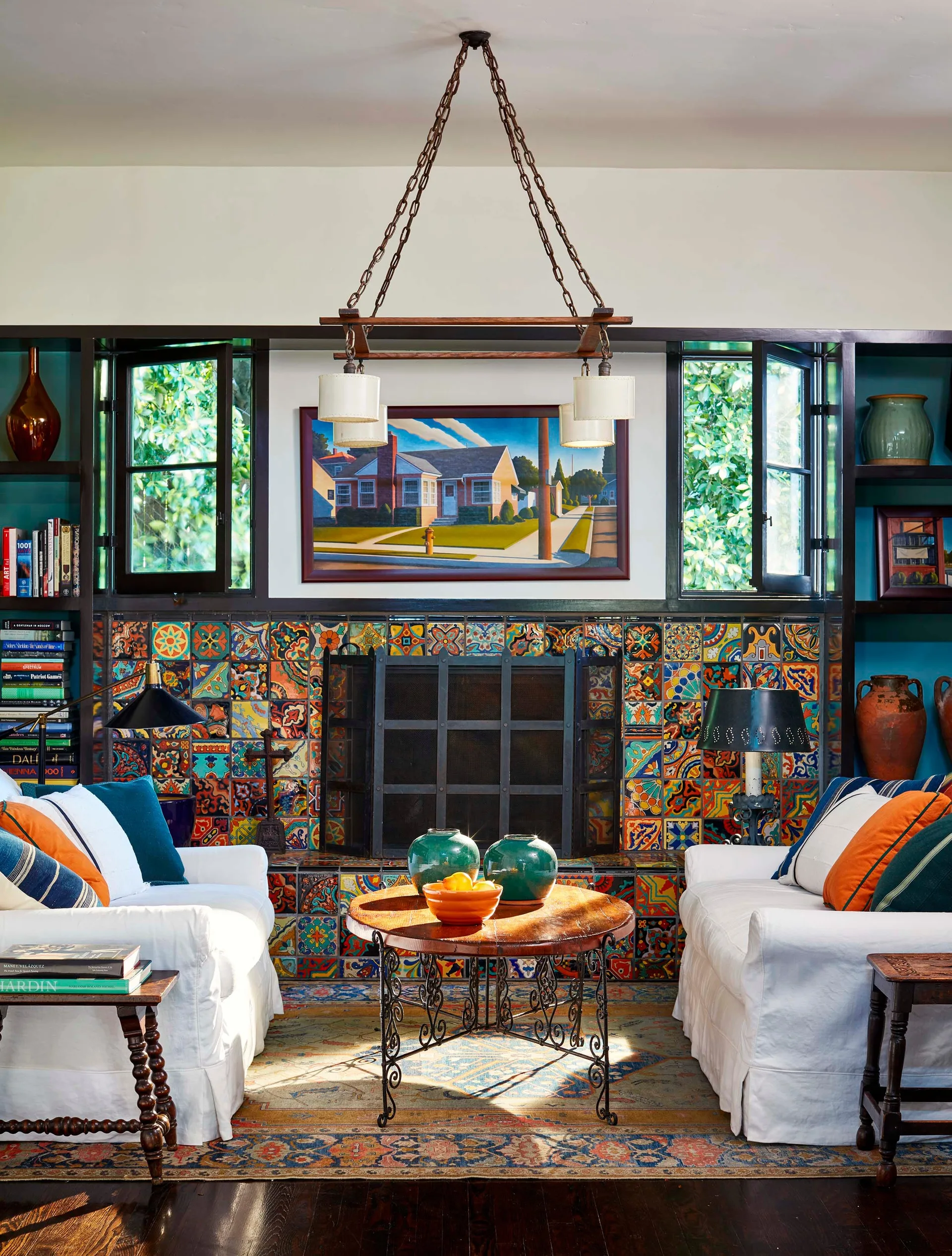 Two white sofas face a vibrant patterned tile fireplace flanked by dark wood built-in bookshelves and casement windows.
