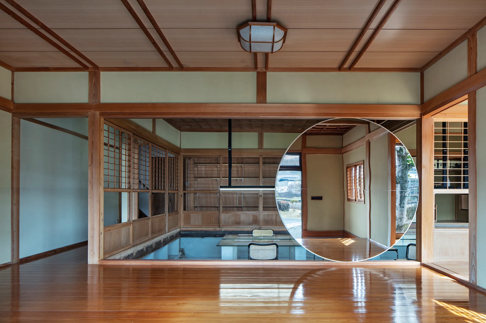 A traditional Japanese room features highly polished wood floors, exposed timber framing, and a large circular mirror reflecting a modern dining set.