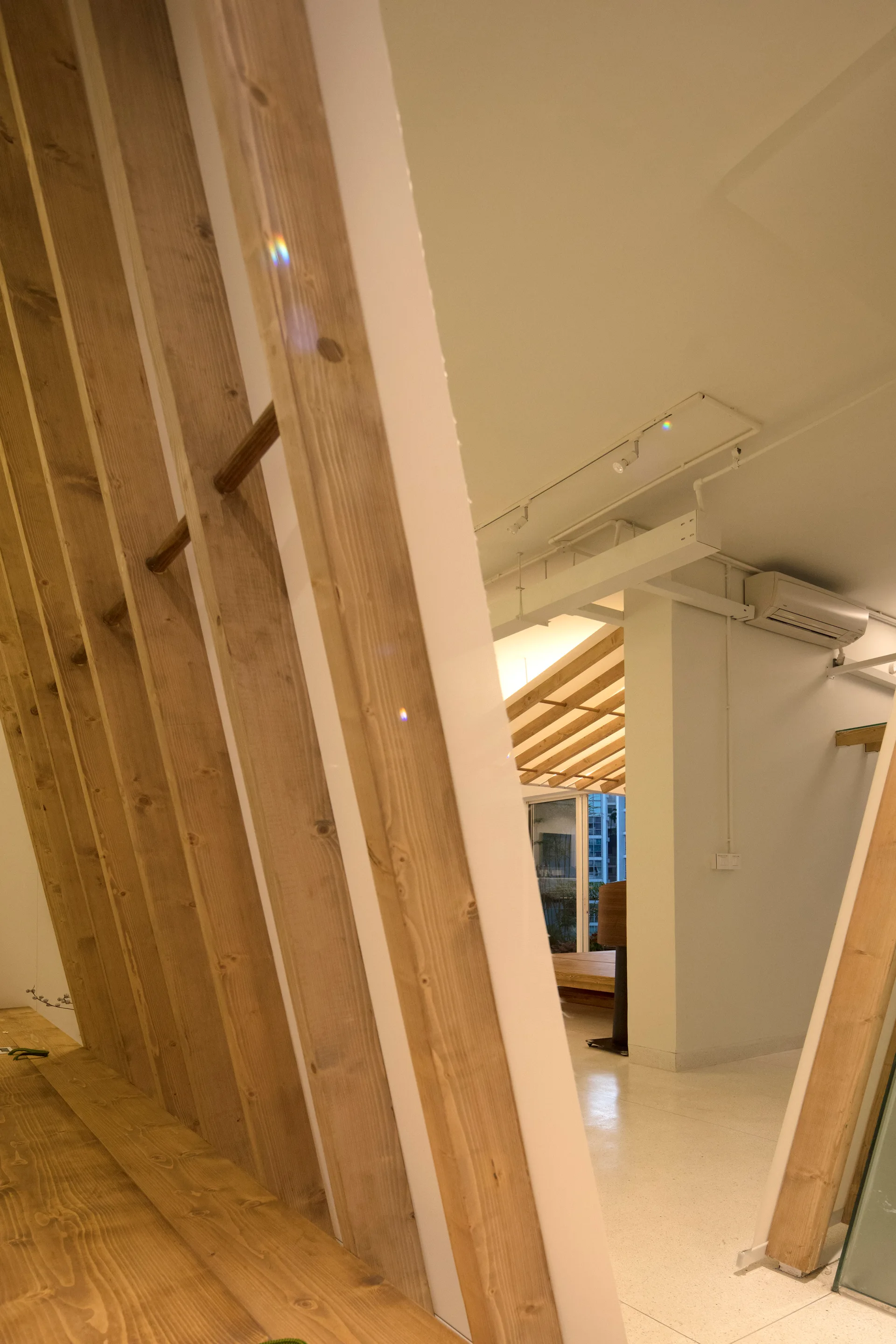 A minimalist interior featuring a vertical light wood slat partition next to a smooth white wall and exposed white ceiling beams.