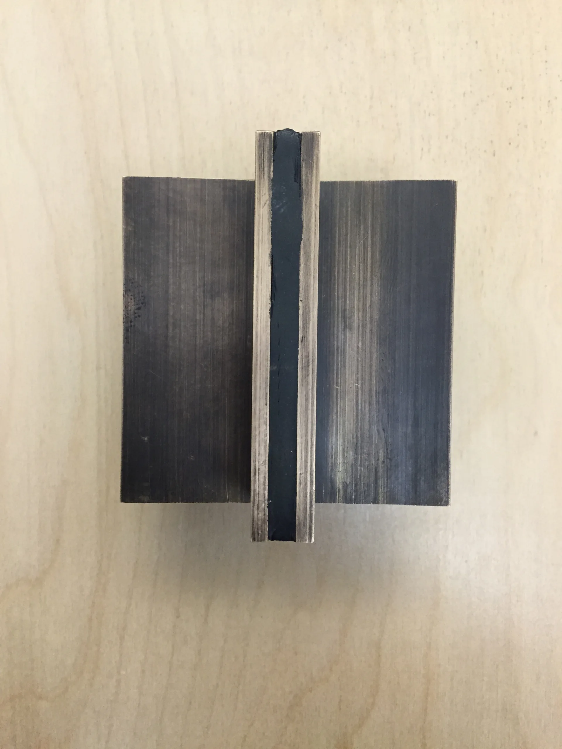 A top-down view of a modern brushed bronze cabinet pull with a vertical black stripe inlay, shown on a light wood background.