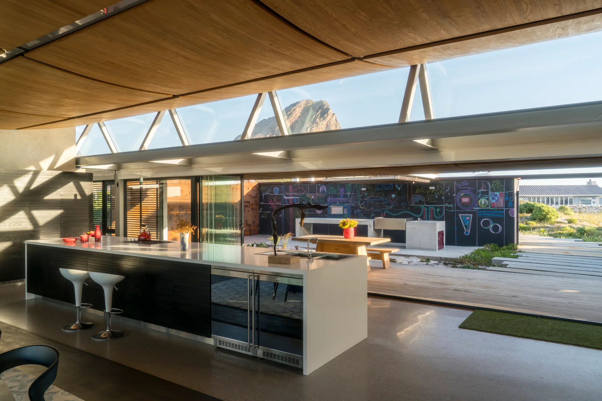 A modern kitchen with a black island, curved wood ceiling, and sliding glass doors opening to an outdoor patio.