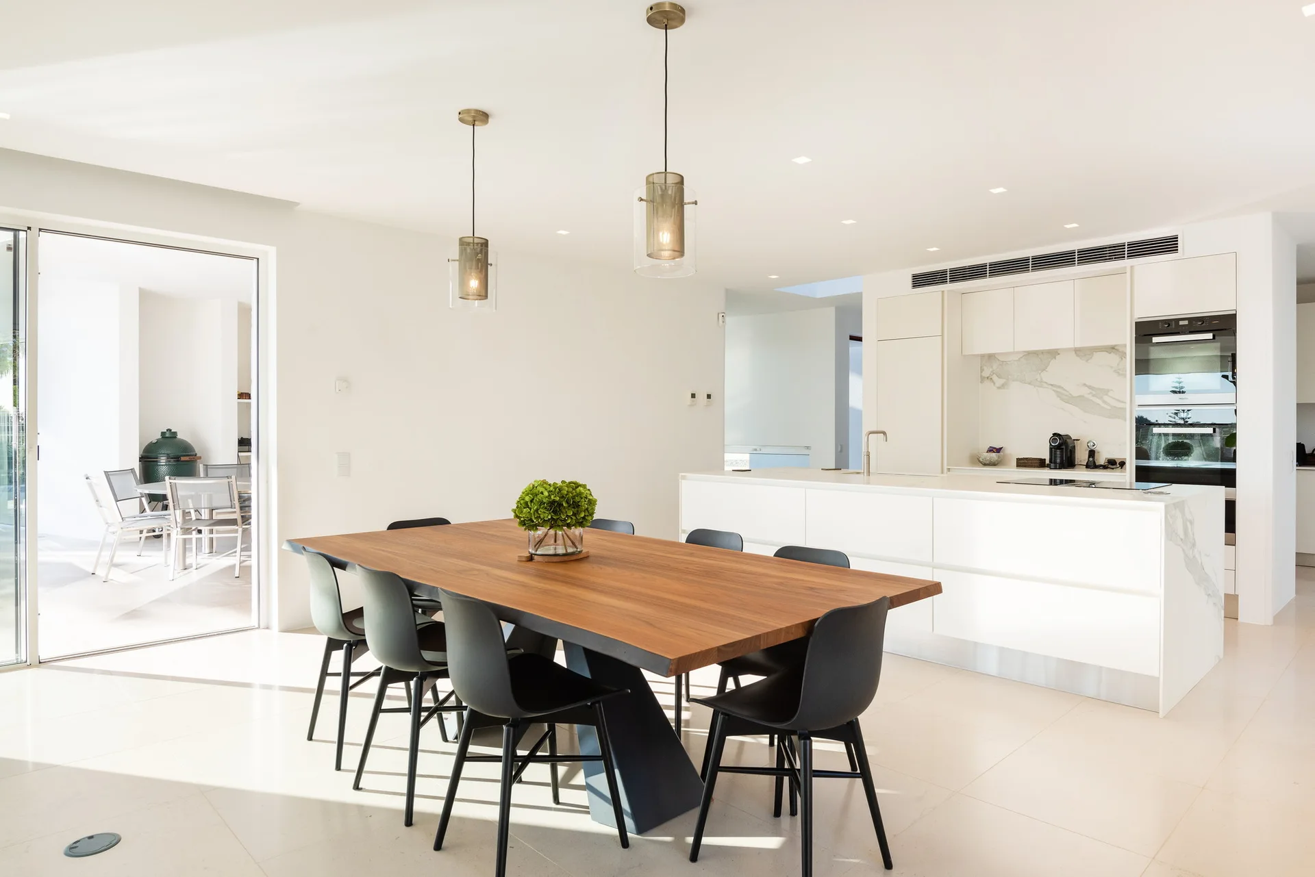 A bright open-concept kitchen features a wooden dining table with black chairs, a white kitchen island, and a sliding glass door.