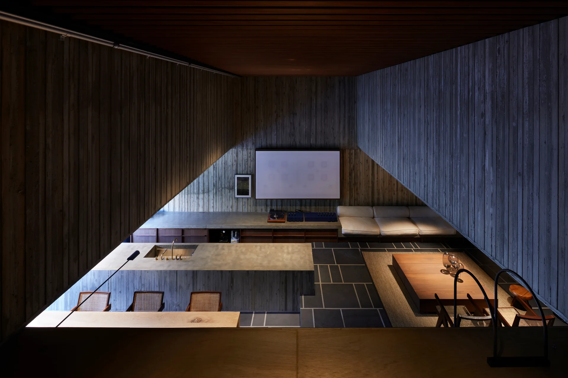 A modern space features board-formed concrete walls, a large concrete kitchen island with a gold faucet, and a sunken living area.
