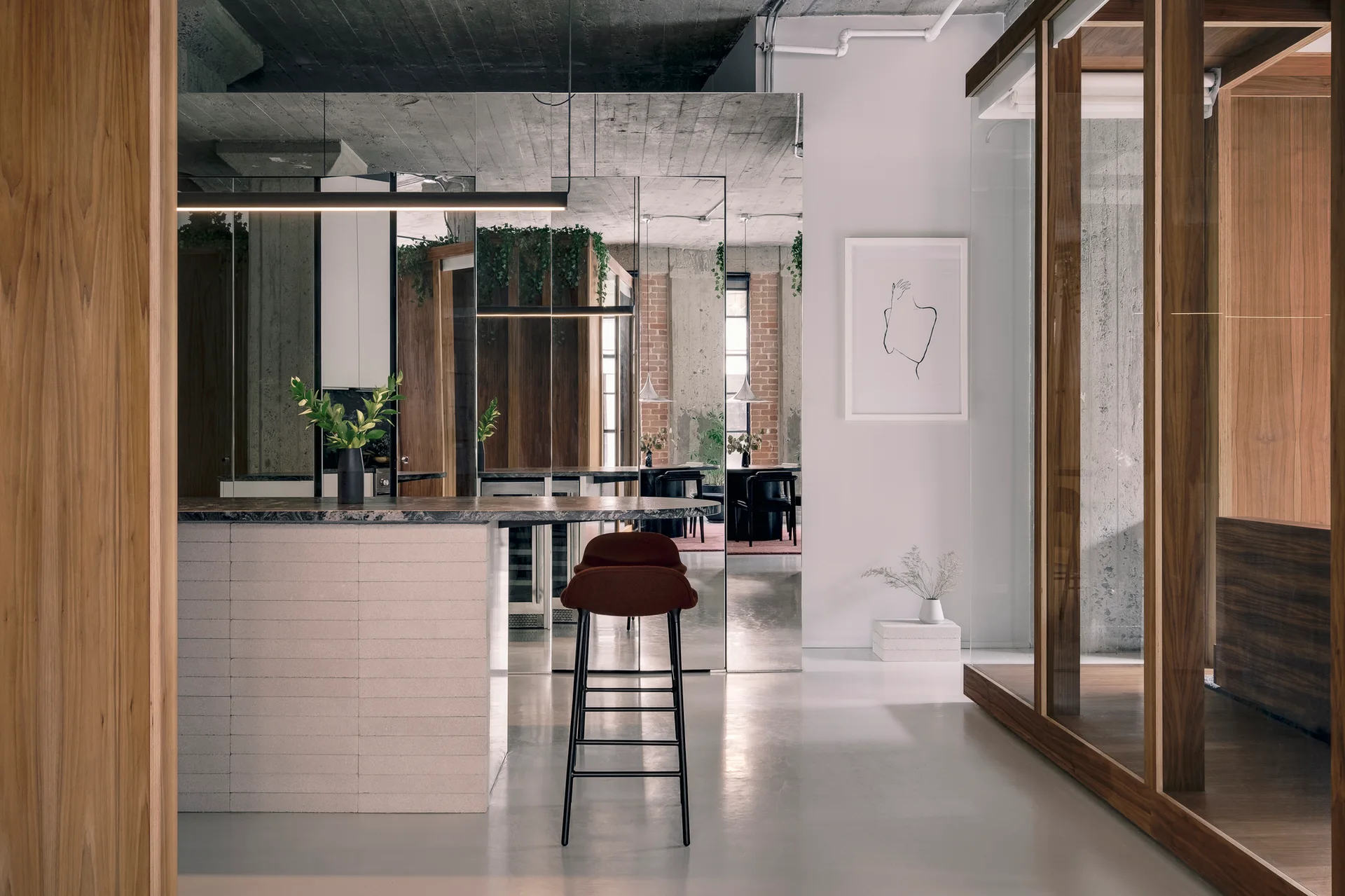 A modern industrial loft kitchen featuring a stone-topped island with one rust bar stool, a concrete ceiling, and a large mirrored partition wall.