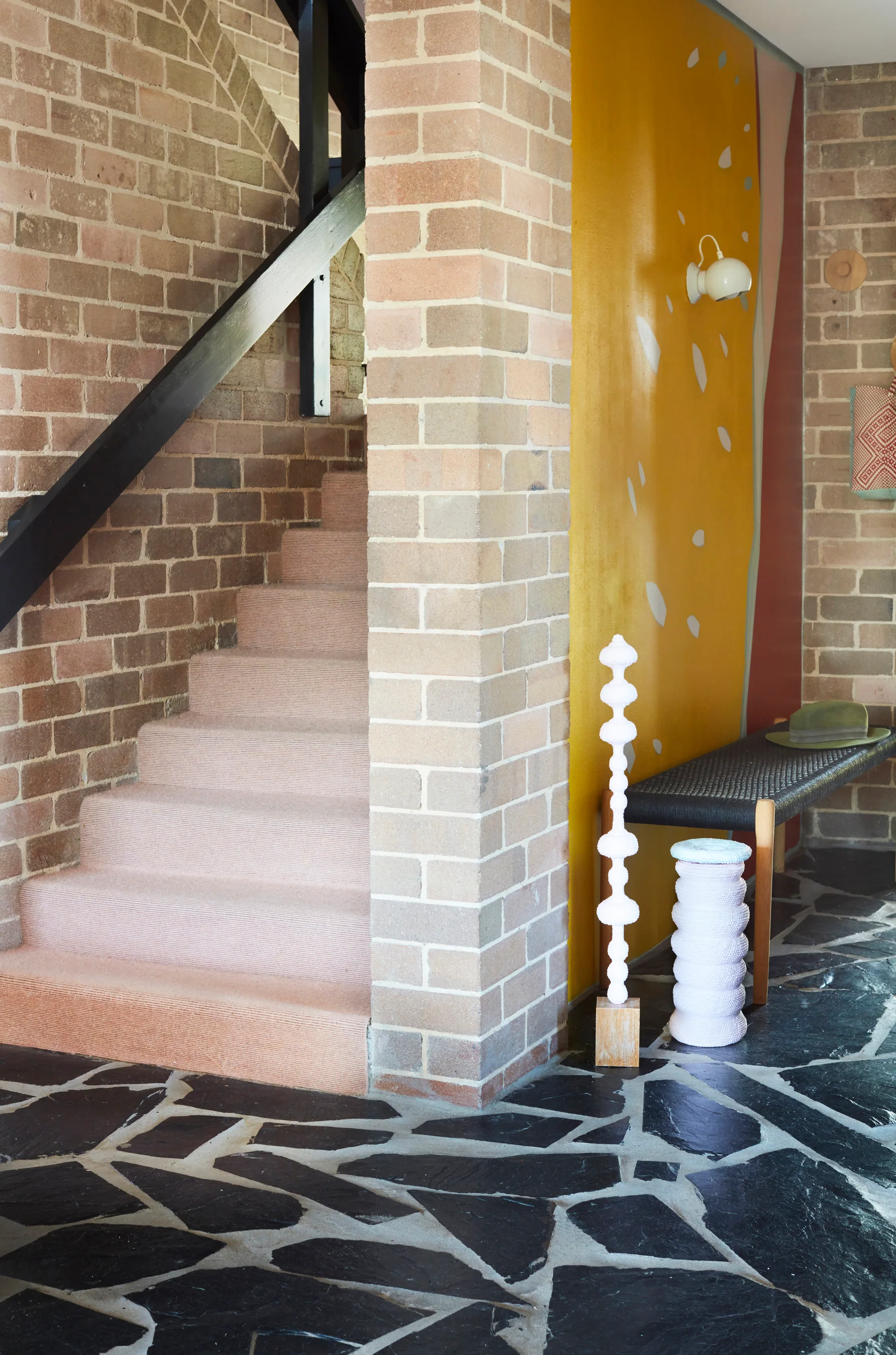 An entryway featuring a brick staircase with pale pink carpeting, a dark flagstone floor, and a bright yellow painted accent wall.