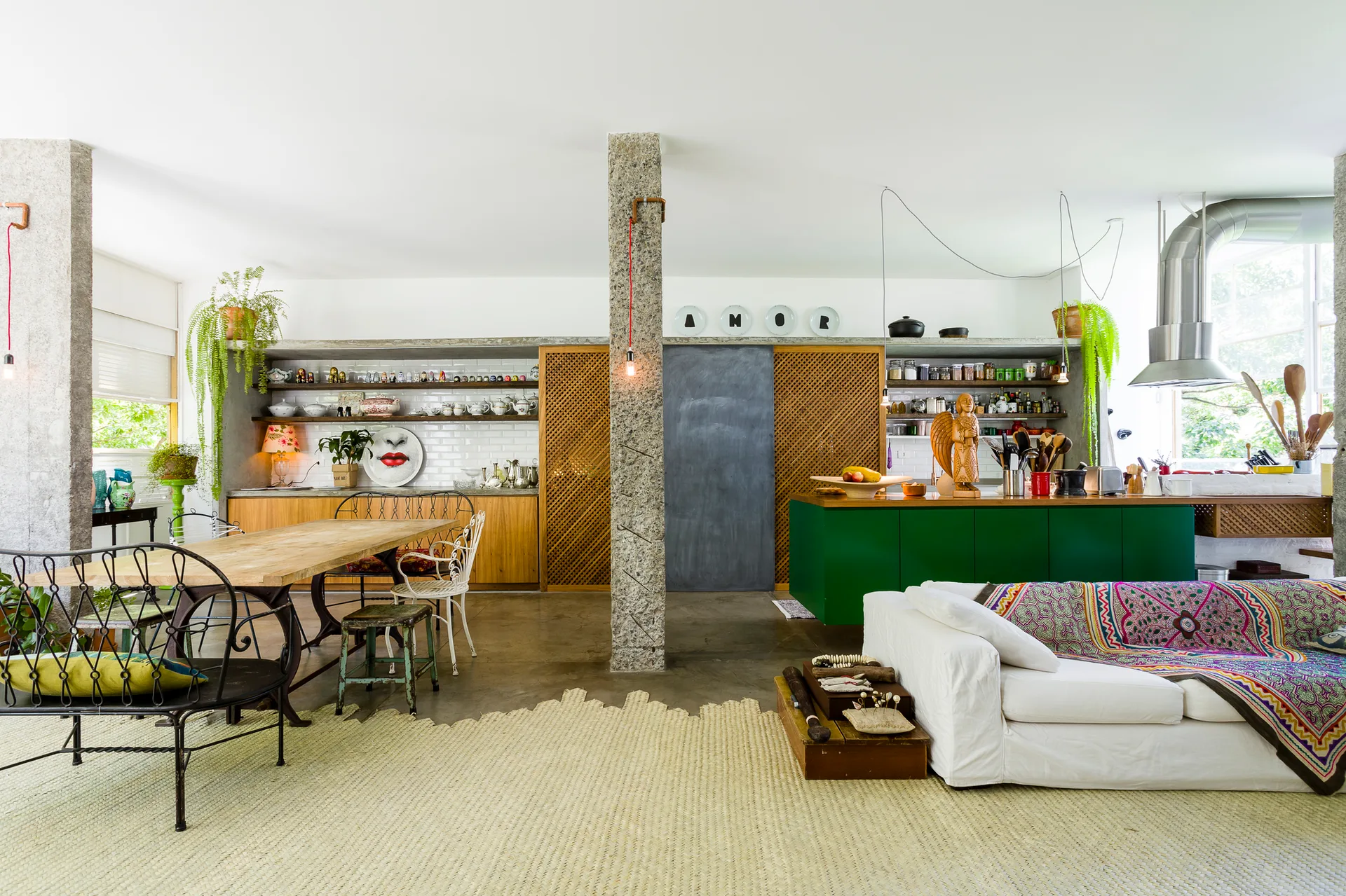 An open concept living and dining area with exposed stone columns, a white sofa, mismatched dining chairs, and a vibrant green kitchen island.