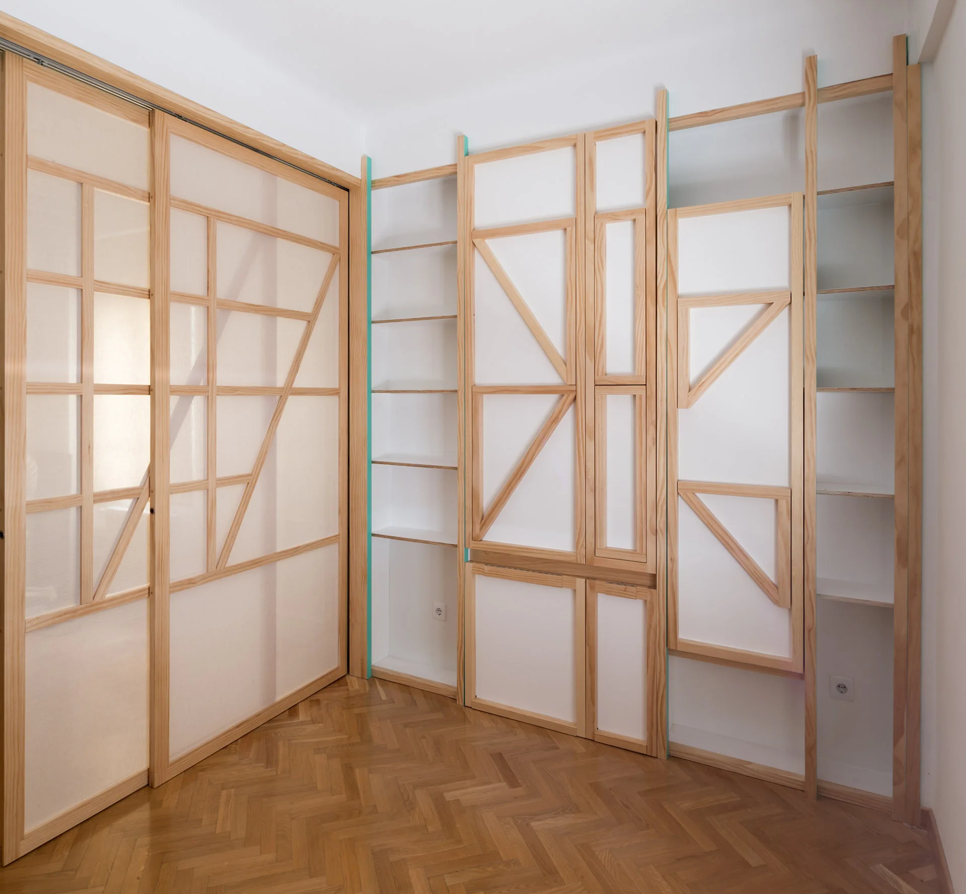 Custom light wood sliding doors and open shelving cabinets stand on a herringbone parquet floor next to white walls.
