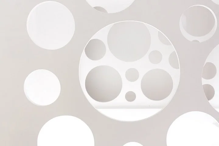 A close-up of a white metal staircase railing panel featuring circular perforated cutouts of varying sizes.