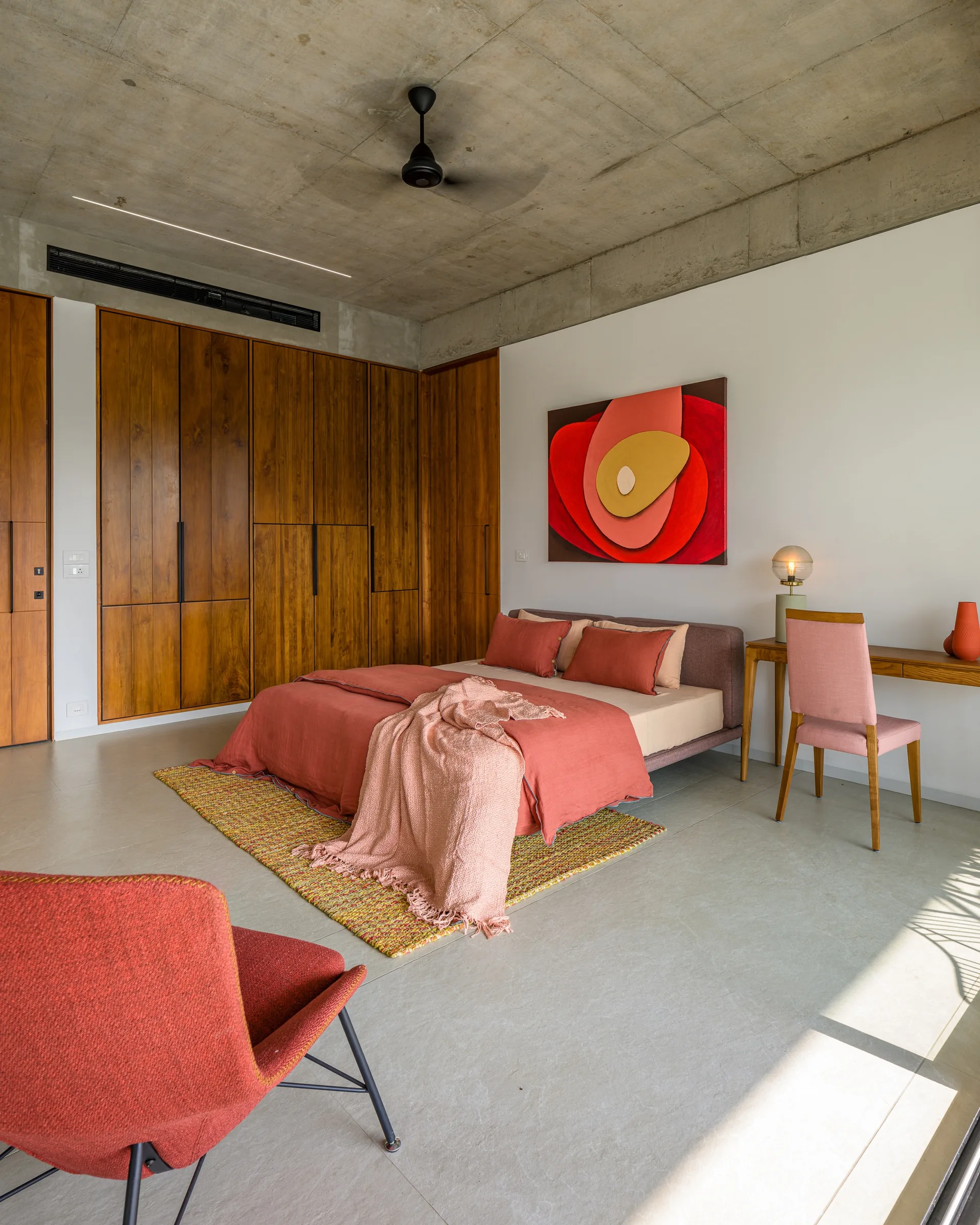 A contemporary bedroom with an exposed concrete ceiling, a large wood-paneled closet wall, and bedding in warm terracotta tones.