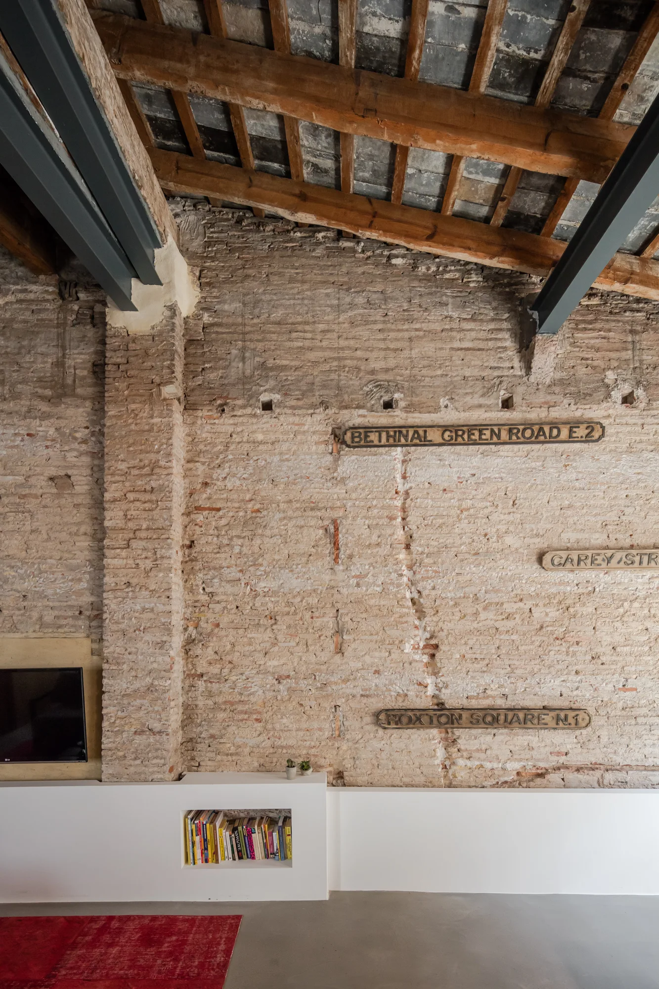 An industrial loft features a raw brick wall decorated with vintage street signs above a low-profile white media unit with a small bookcase.