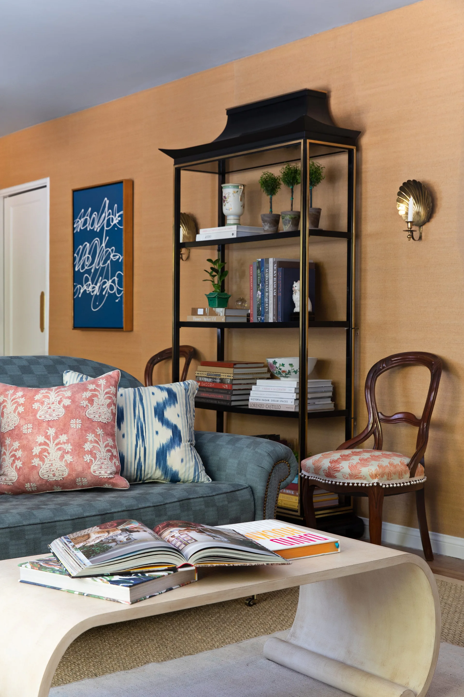 A blue patterned sofa with decorative pillows sits in front of a black pagoda-topped etagere against a textured tan wallpapered wall.