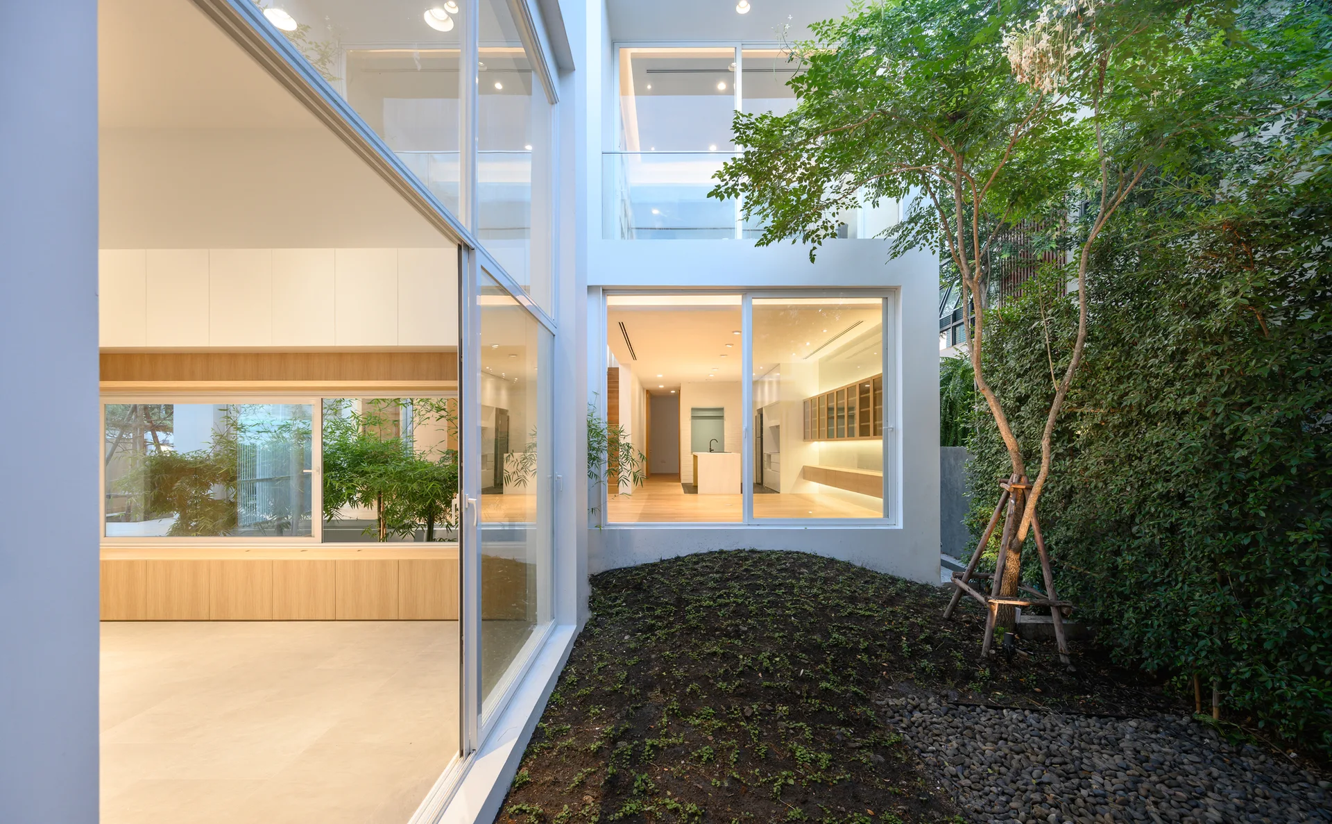 A modern home interior with floor-to-ceiling glass walls looking out onto a central courtyard garden with a small tree.