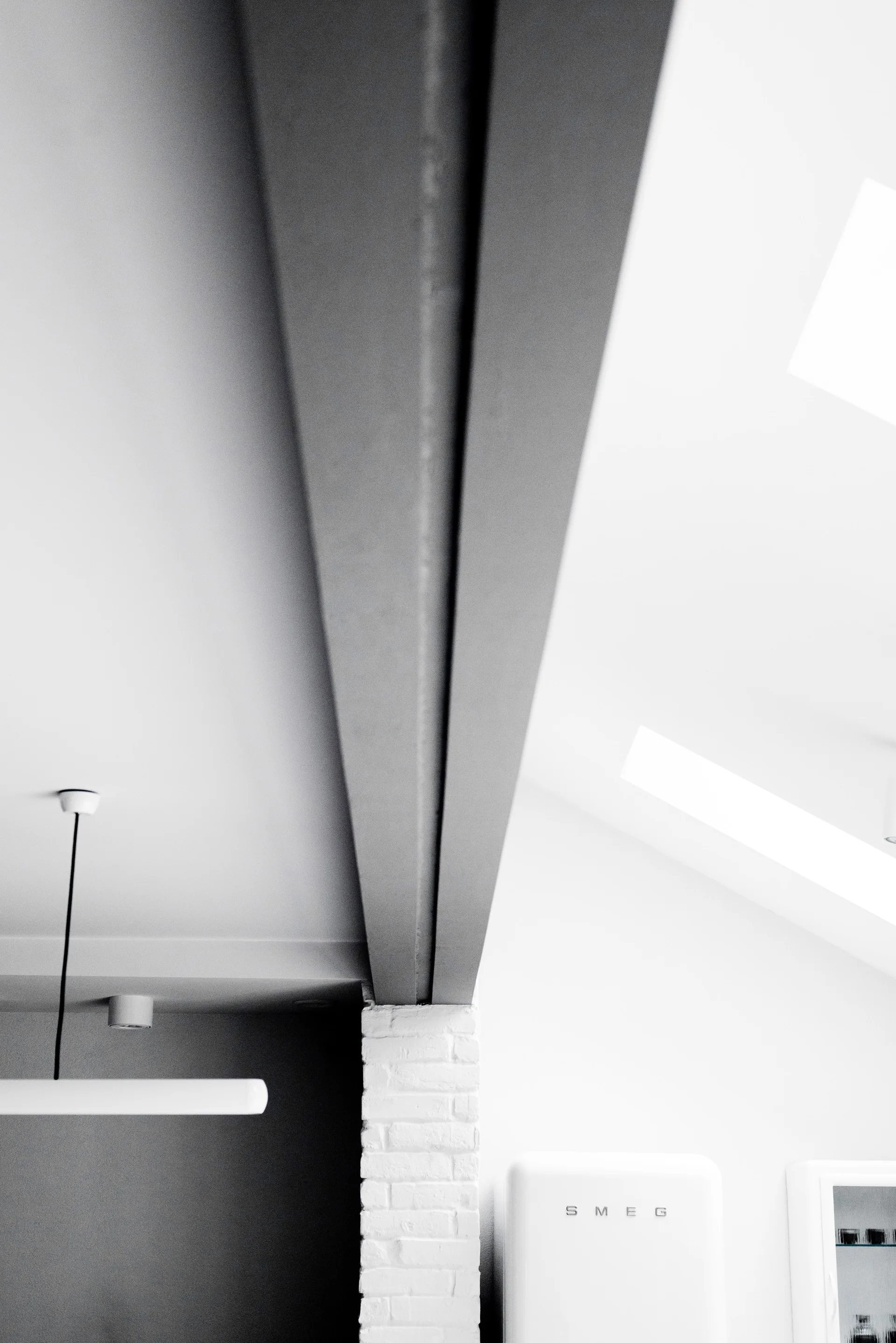 A structural grey ceiling beam rests on a white painted brick column in a modern kitchen with a Smeg refrigerator.
