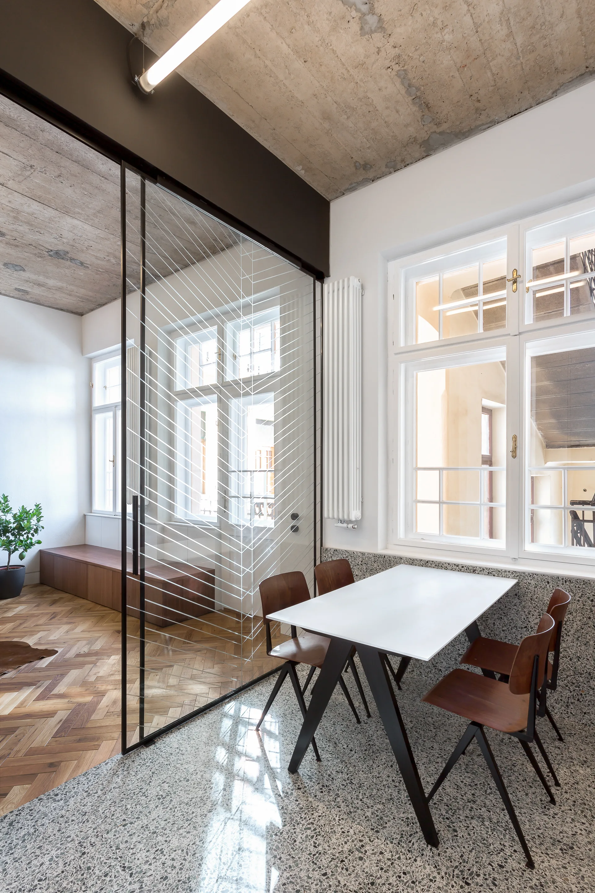 A modern dining room features a white table and wooden chairs on speckled grey terrazzo flooring next to a patterned glass sliding partition.