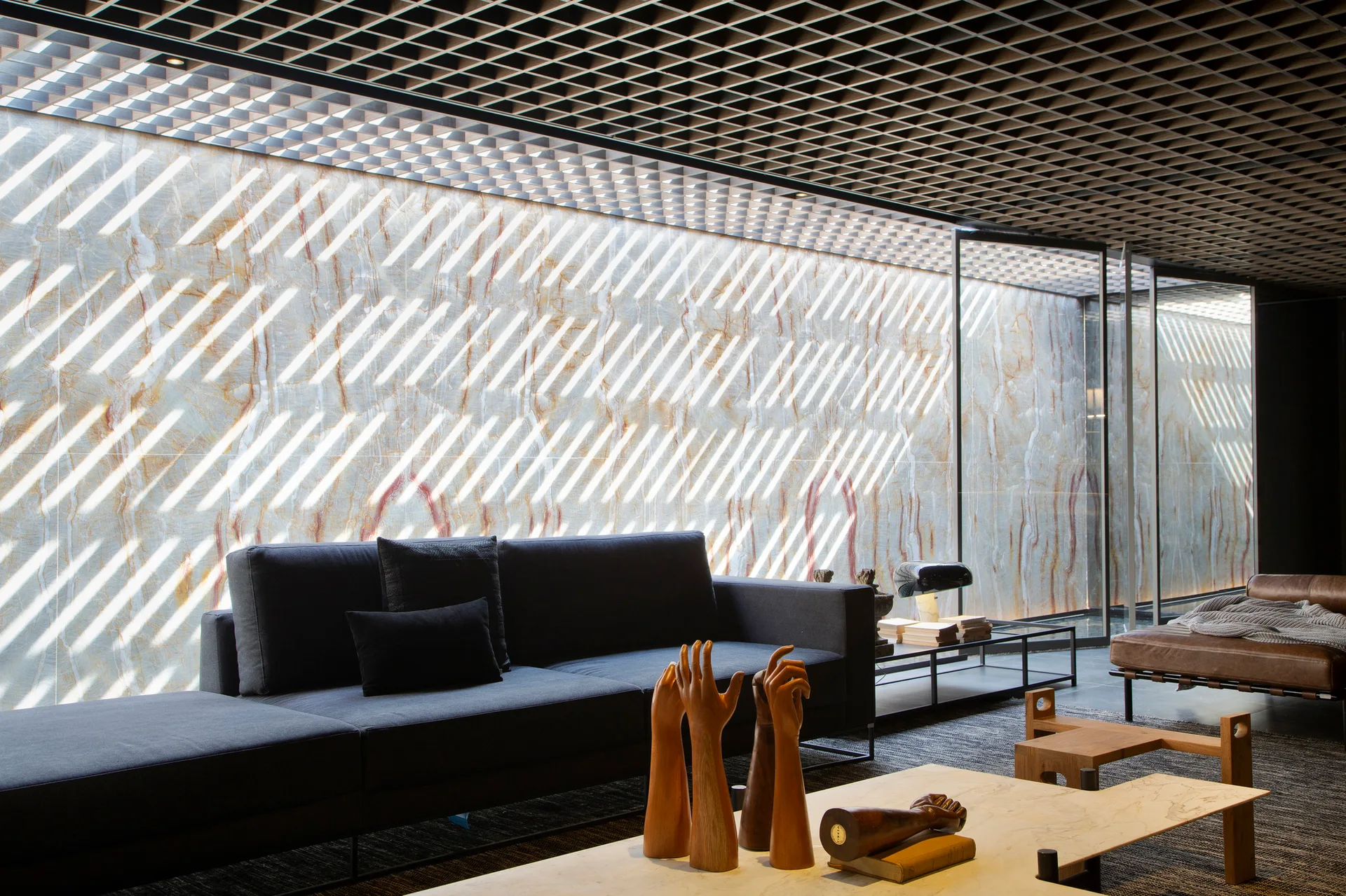 A modern living room featuring a dark sofa set against a backlit stone accent wall under a black grid ceiling.