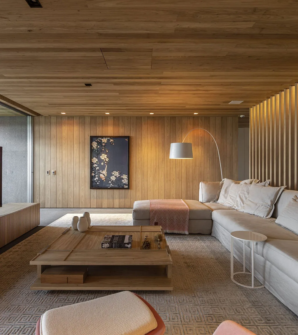 A living room features warm wood-paneled walls and ceiling, a large beige sectional sofa, a low wooden coffee table, and an arched floor lamp.