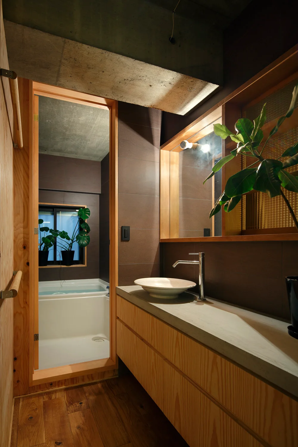 A modern bathroom vanity made of light wood with a concrete countertop, vessel sink, and a view into a secondary bathing space.