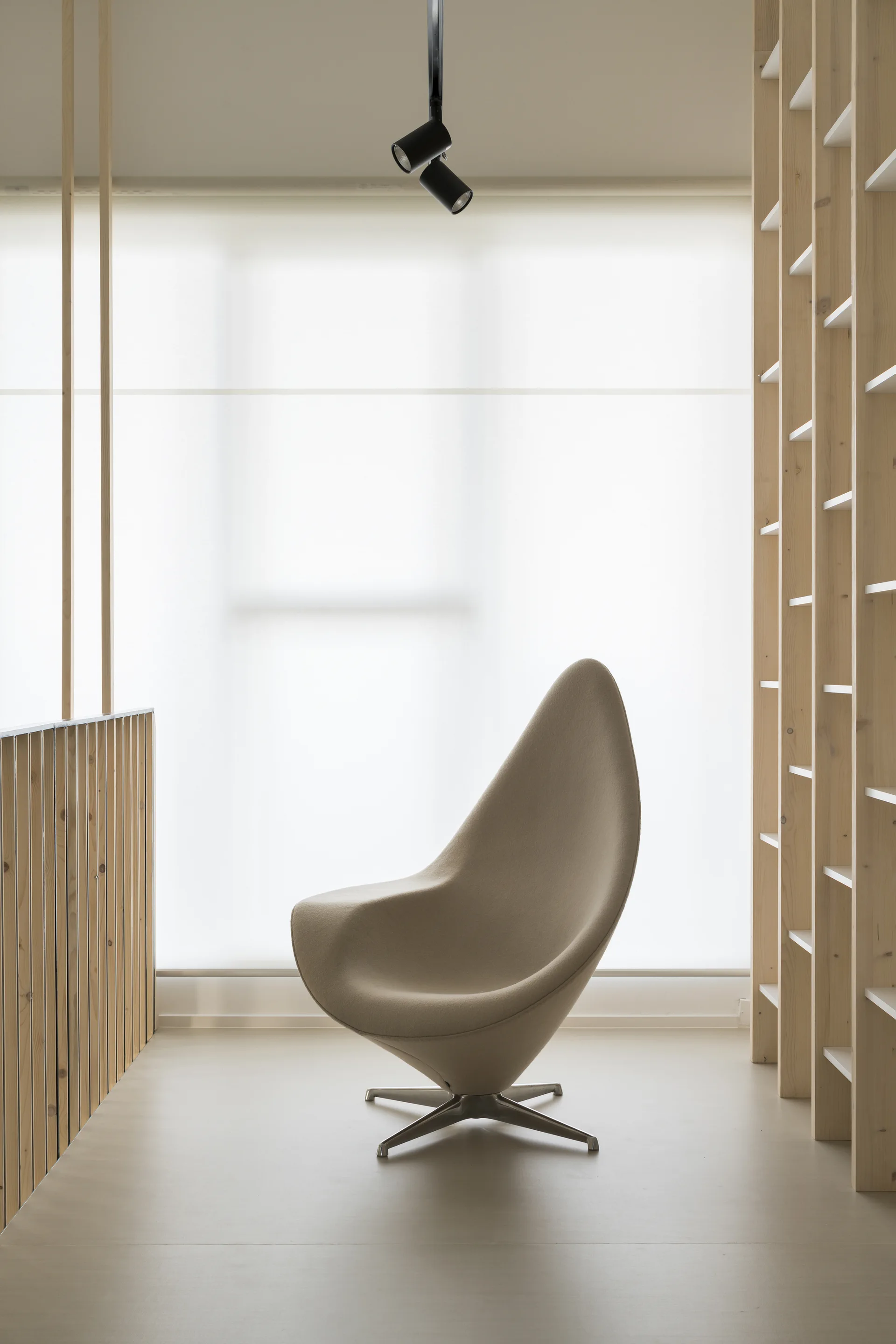 A sculptural beige fabric accent chair stands in a minimalist room with a light wood slatted partition and built-in shelving.