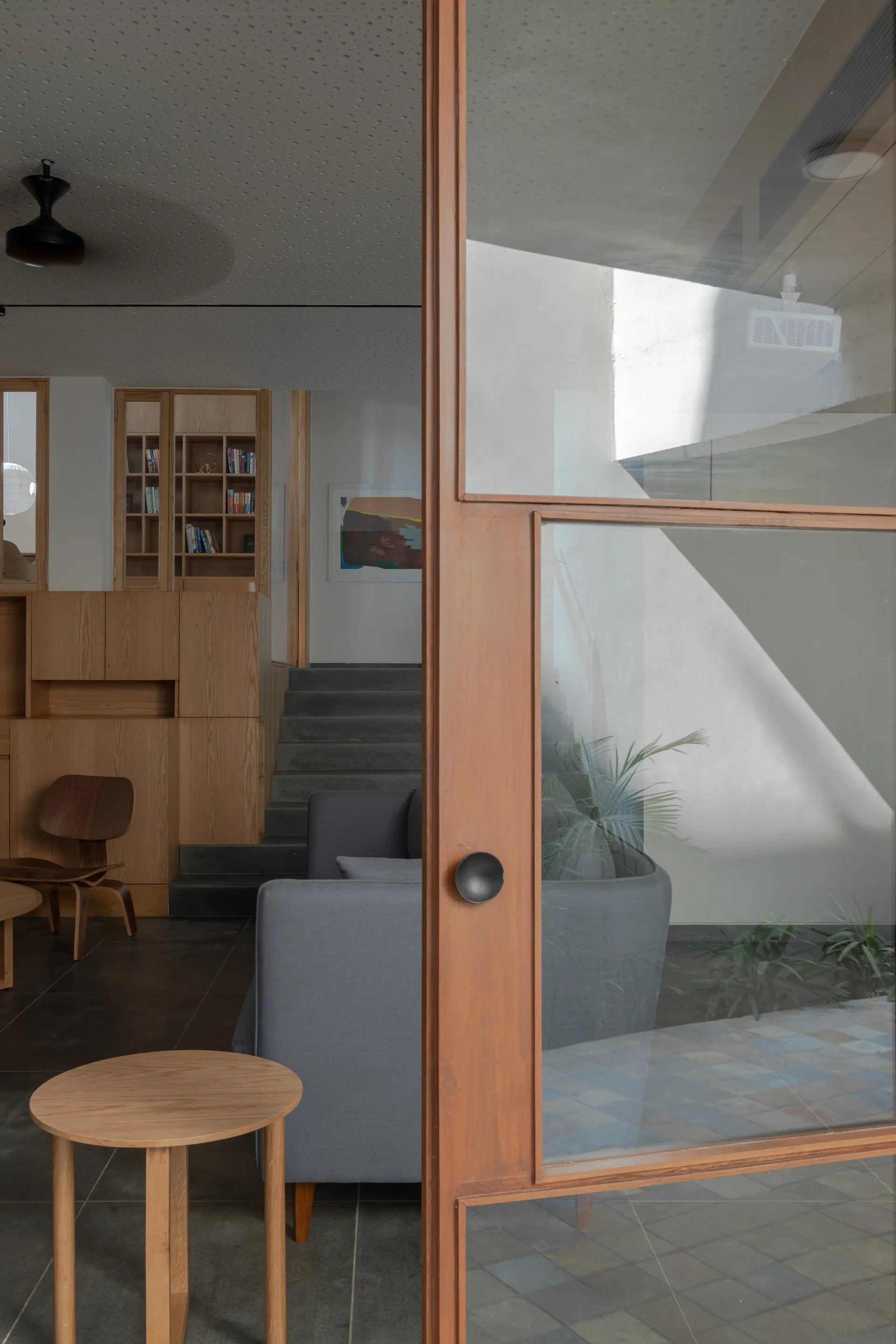 A view through a wood-framed glass door into a living room featuring a grey sofa, a small round wooden side table, and stone stairs in the background.