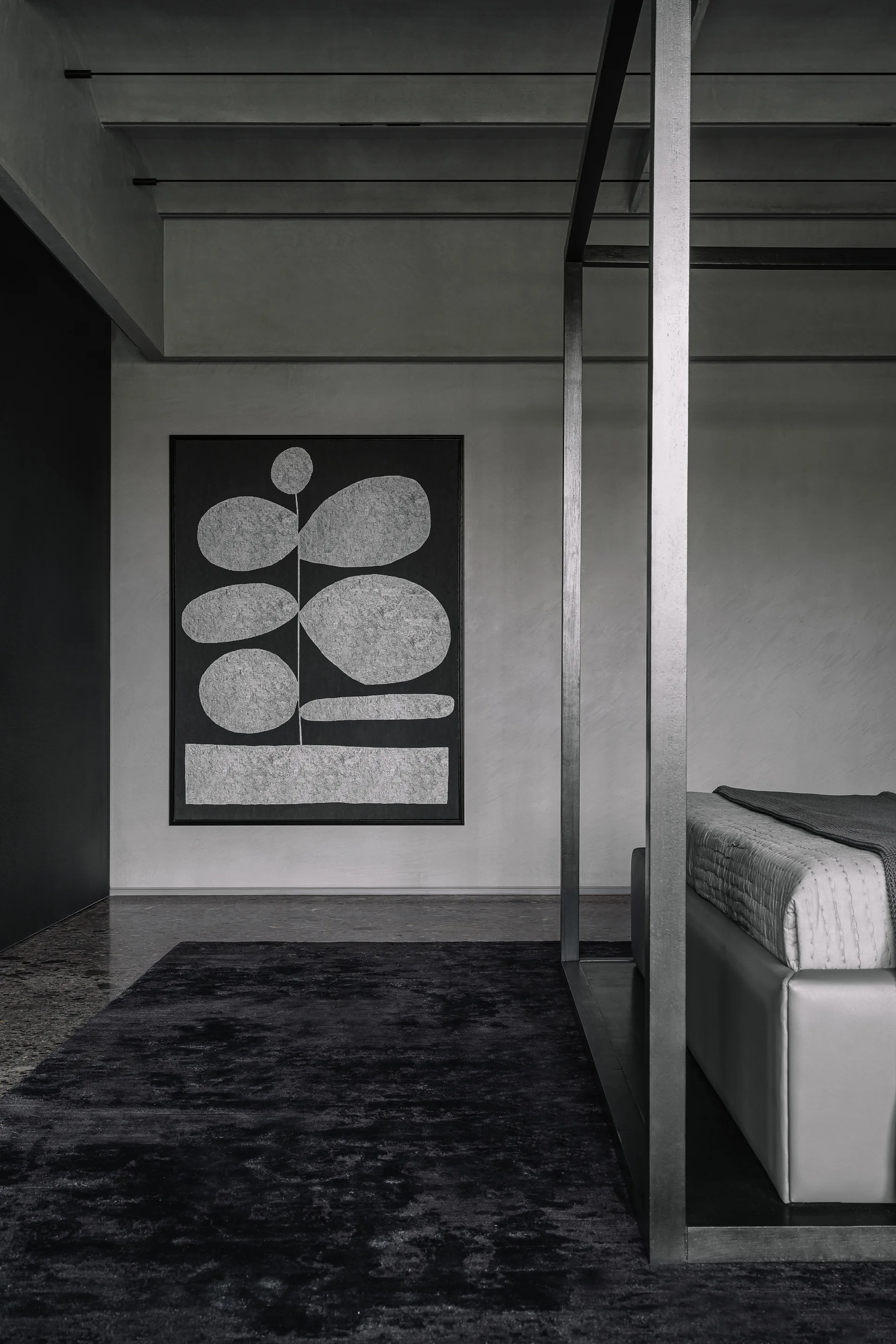 A monochromatic gray bedroom featuring a metallic canopy bed frame, a large black and white abstract painting, and a dark textured rug.